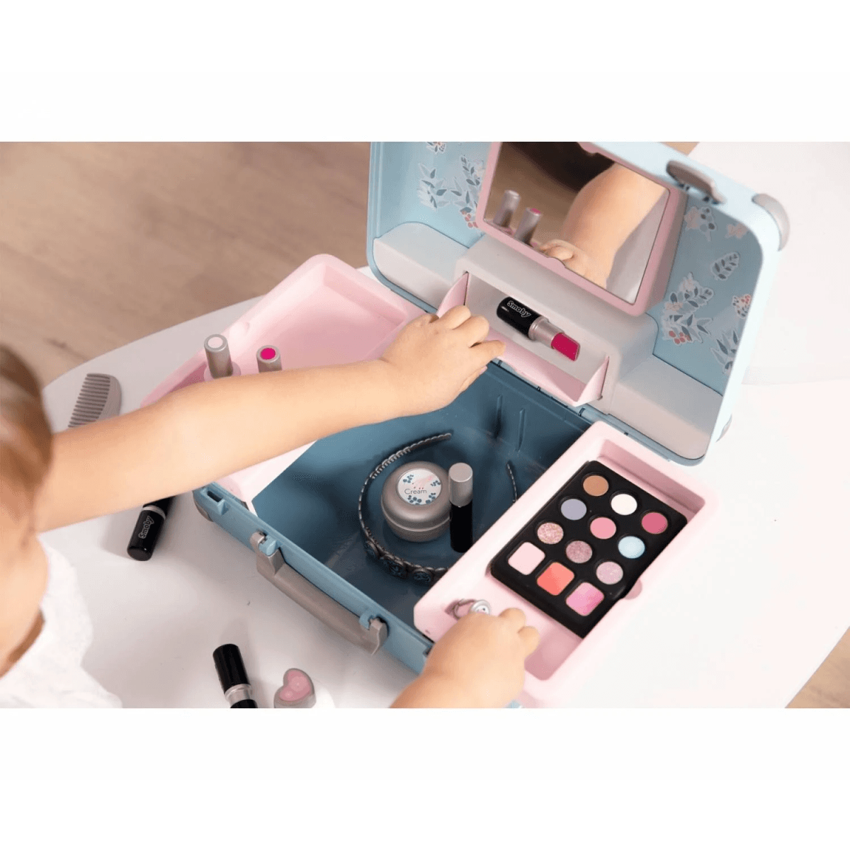 Ein Kind spielt mit einem Spielzeug-Schminkkoffer mit Lippenstiften, Lidschatten und Kamm.