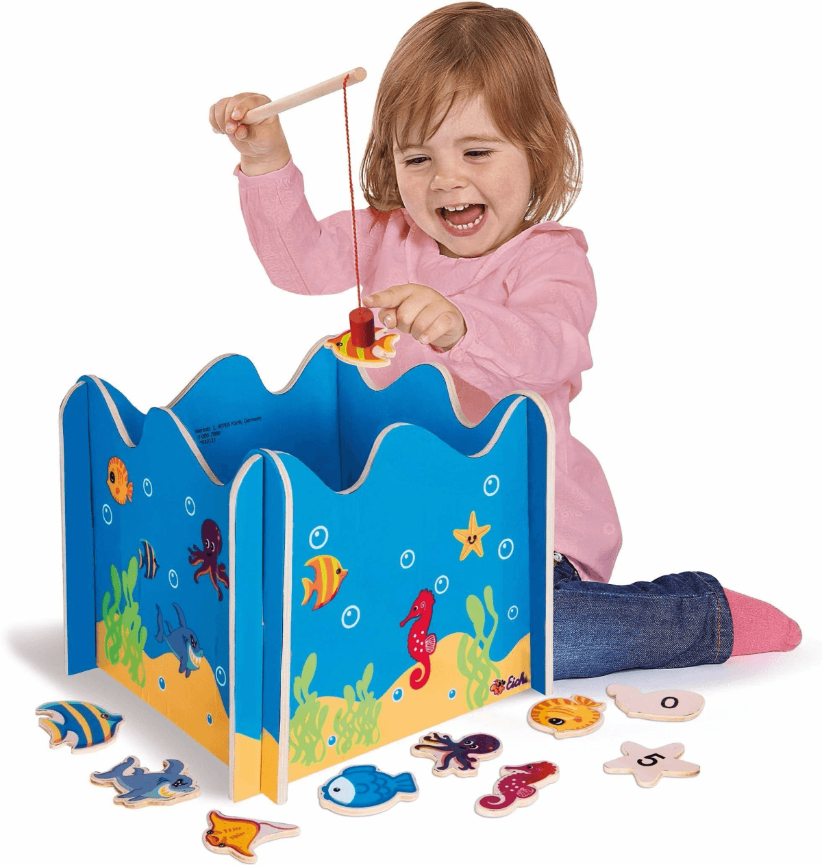 Ein kleines Mädchen angelt mit einer Angel und einem Holzfisch an einem blauen Spielzeug.