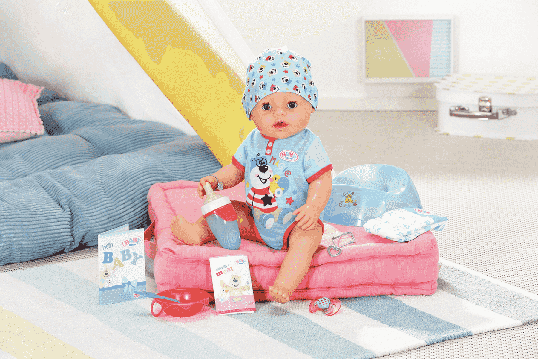 Babypuppe sitzt auf rosa Kissen mit Flasche, Töpfchen und Spielzeug.
