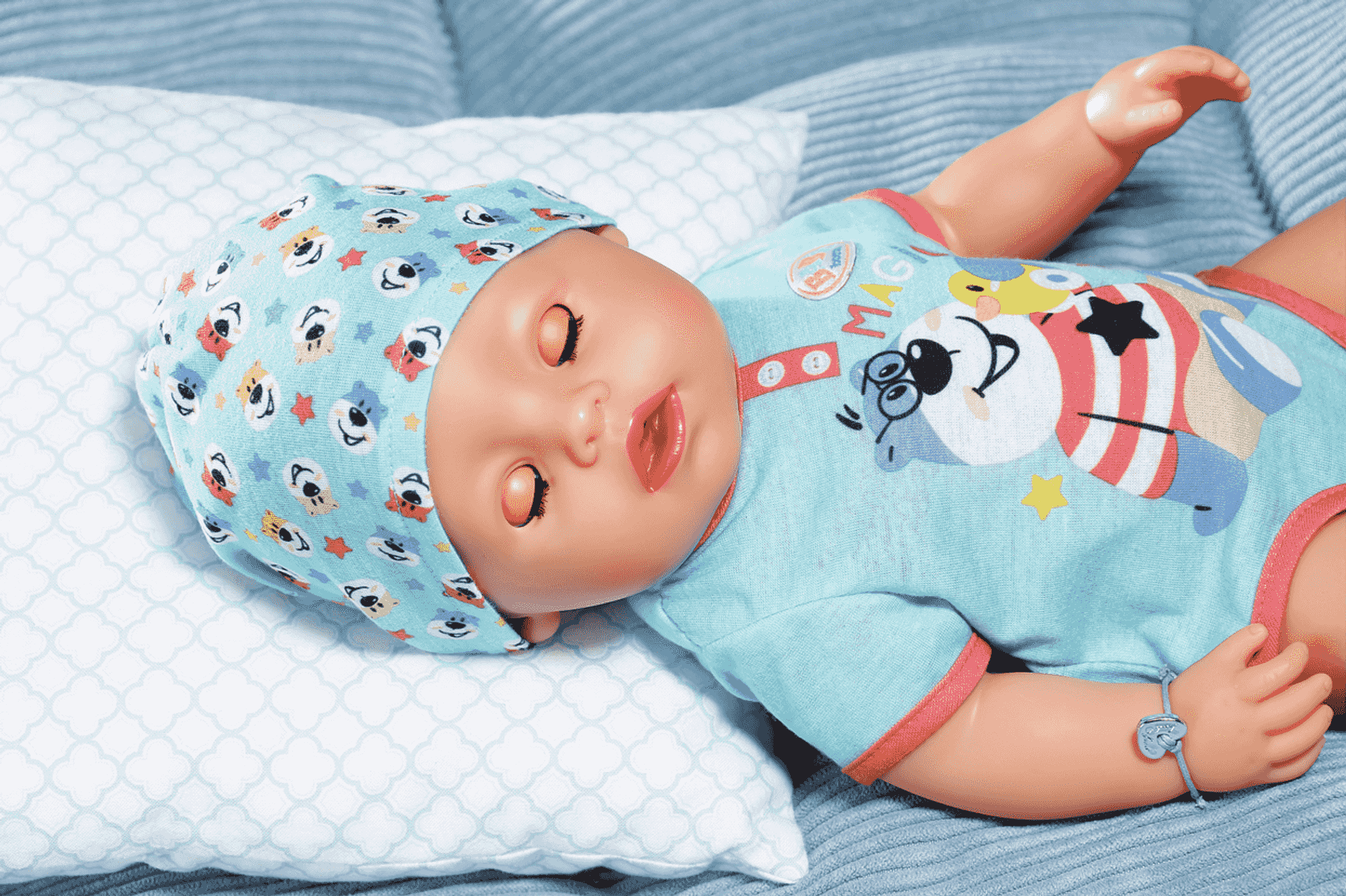 Ein Babykleidungs-Puppen-Schlafanzug mit Bärenmotiv liegt auf einem Kissen.