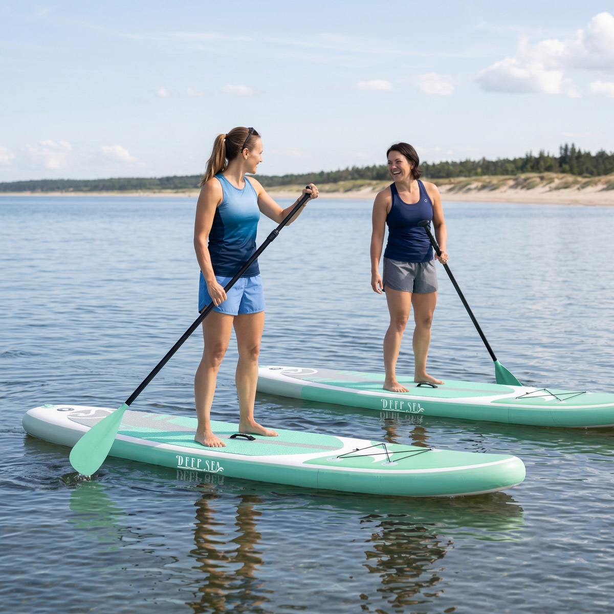 Dwie kobiety na desce do paddleboardingu na wodzie, trzymające wiosła.