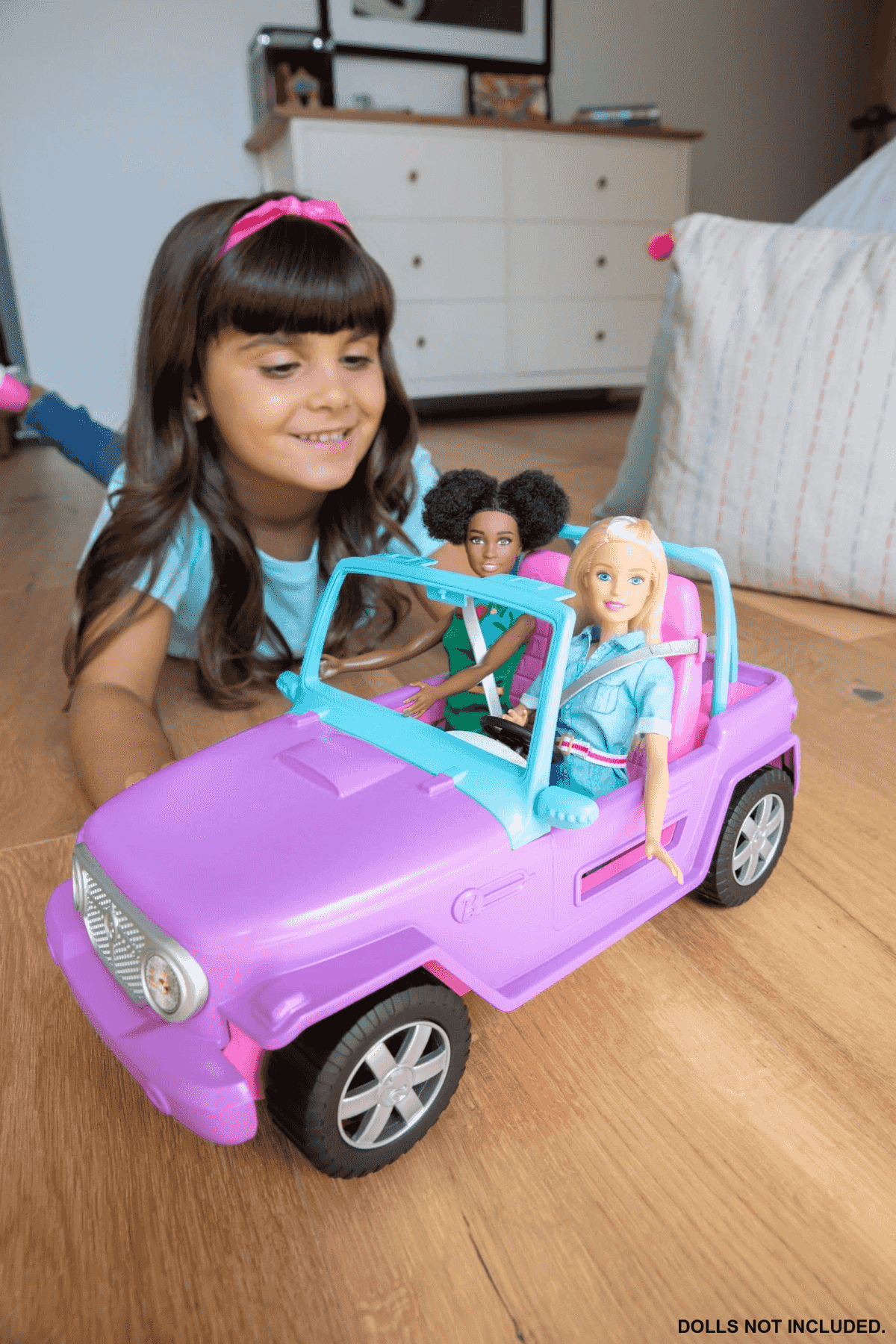 Una niña juega con un coche de juguete morado con dos muñecas dentro.