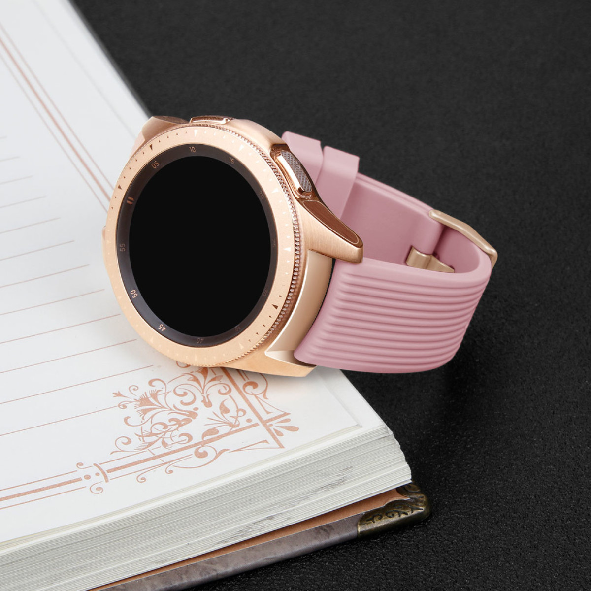 Uno smartwatch rosa con cassa dorata poggia su un taccuino aperto.