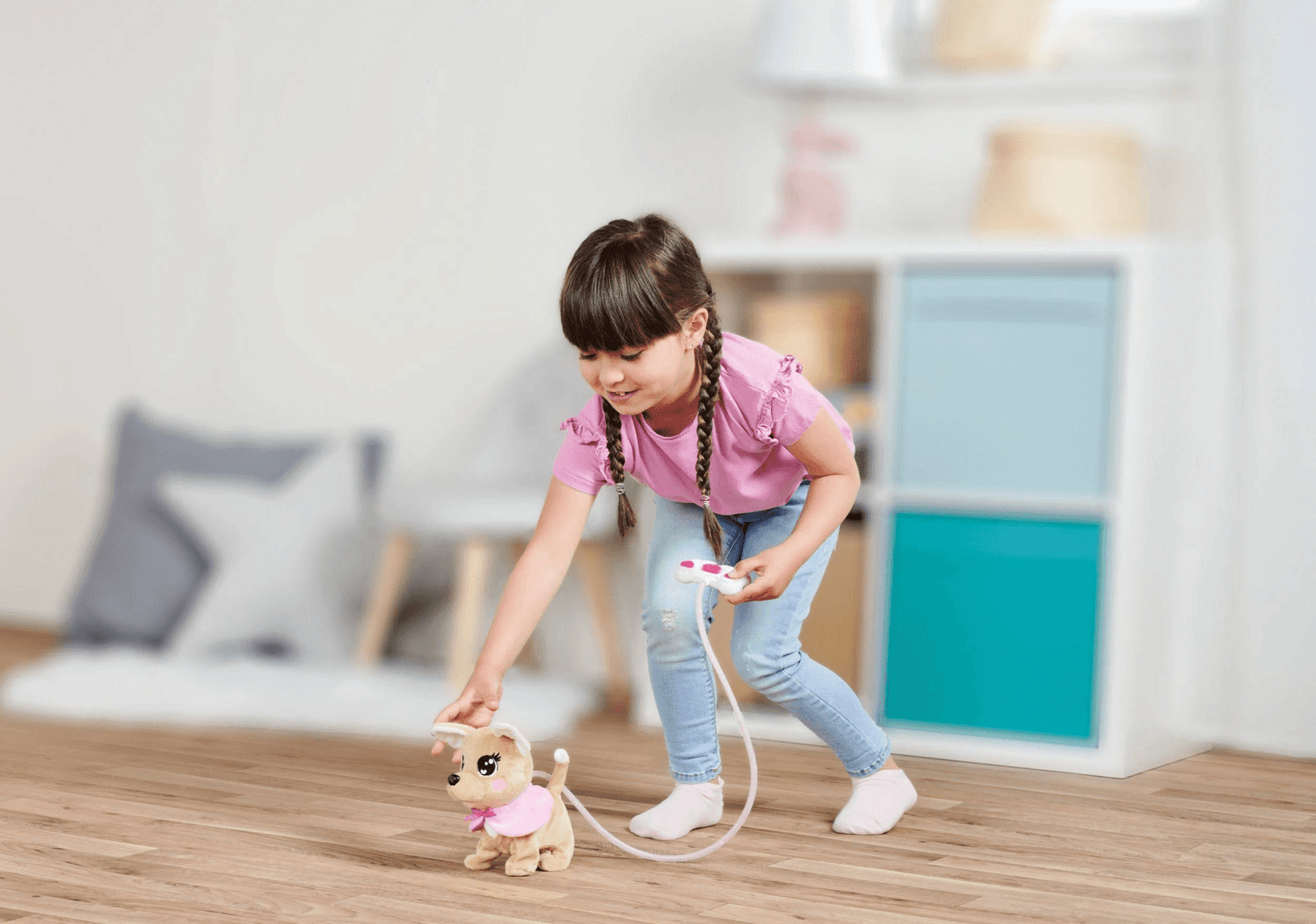 Una niña con camisa rosa y jeans juega con un perro de juguete con correa.
