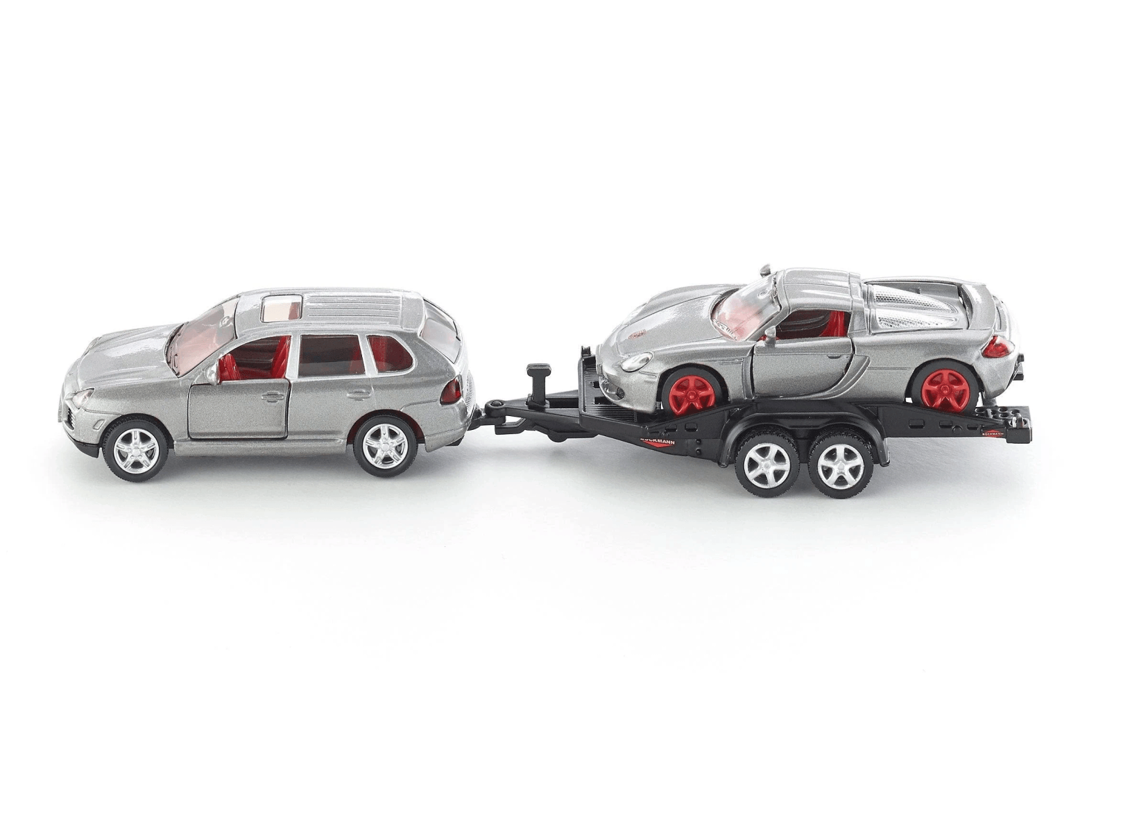 SUV plateado remolcando un remolque con un coche deportivo plateado, interior rojo.