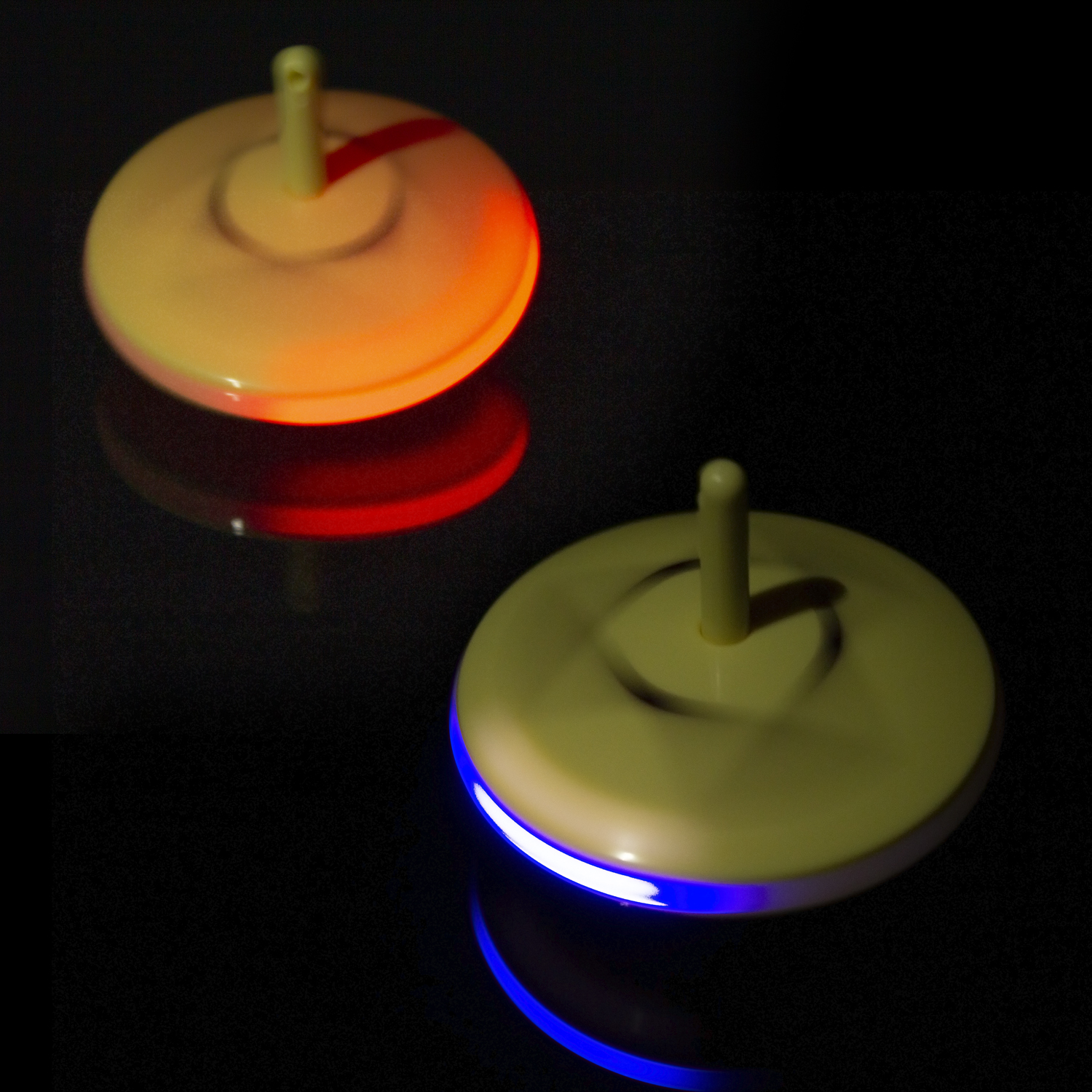 Due trottole luminose, una rossa e una blu, su sfondo scuro riflettente.
