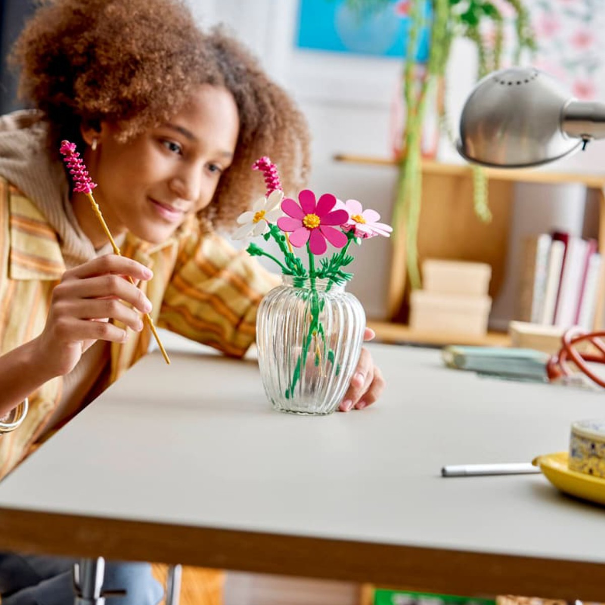Una ragazza con i capelli ricci costruisce un vaso con fiori Lego colorati.