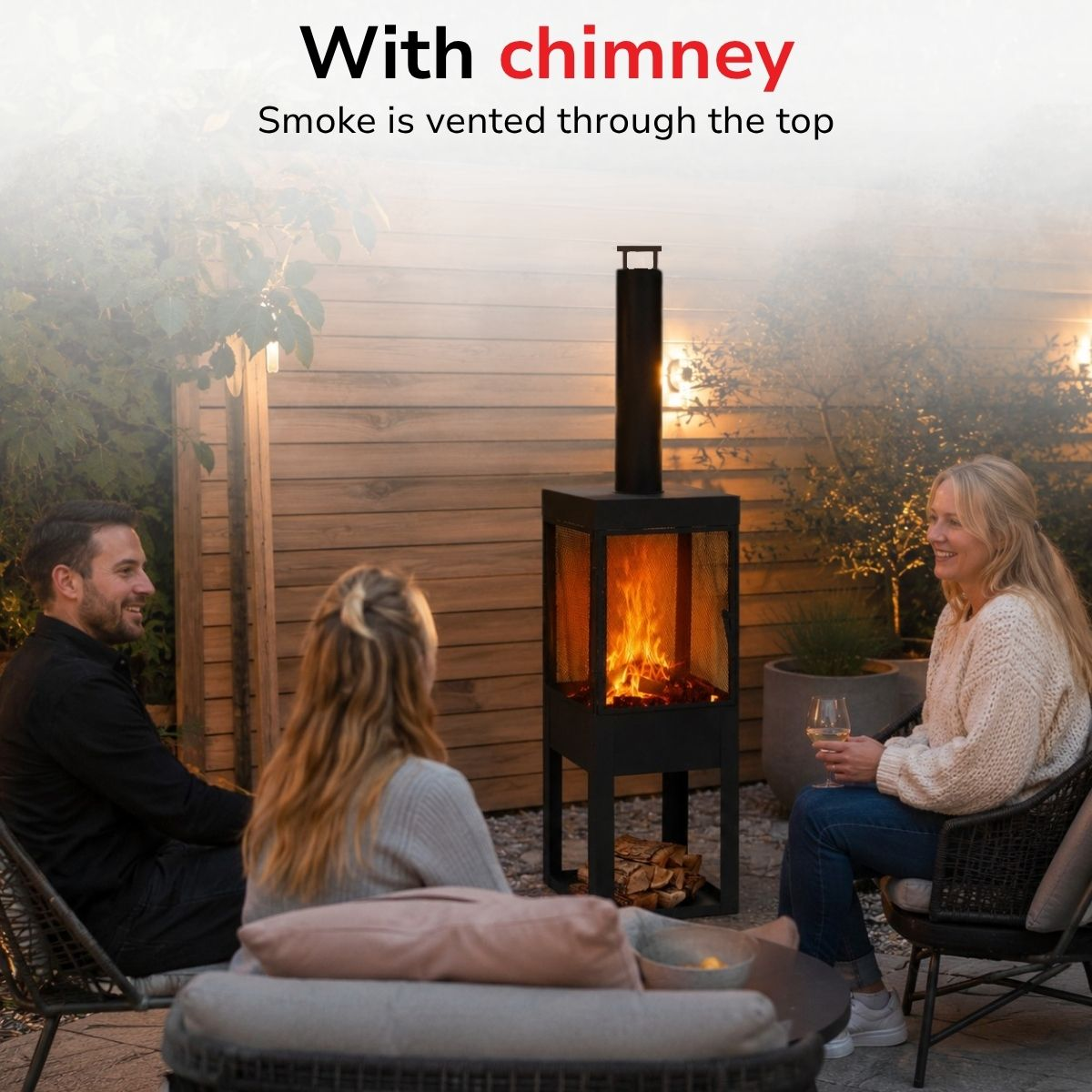 Three people sit around an outdoor fireplace with a chimney.