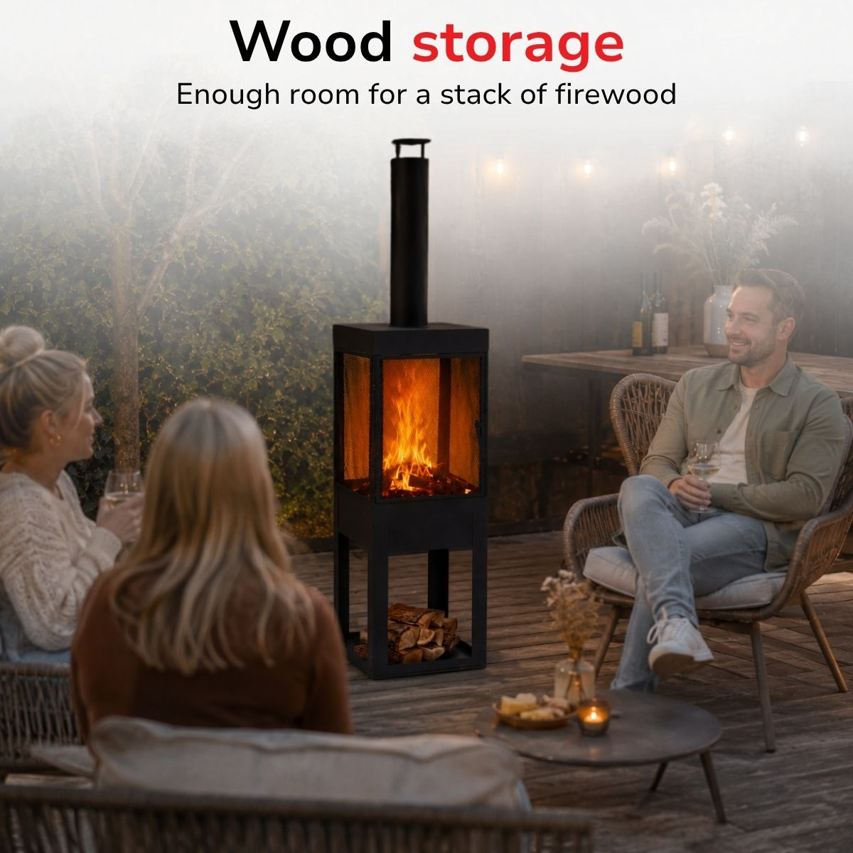 A man and two women sit outdoors around a fire. Wood logs are beside it.
