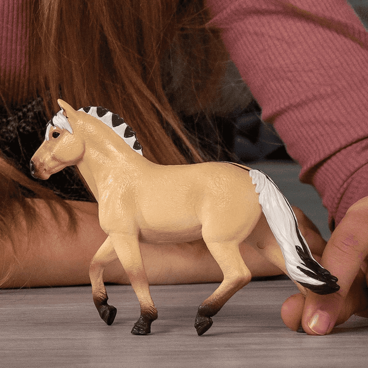 Eine beige Spielzeugpferdestatue mit schwarzer Mähne und weißem Schweif.