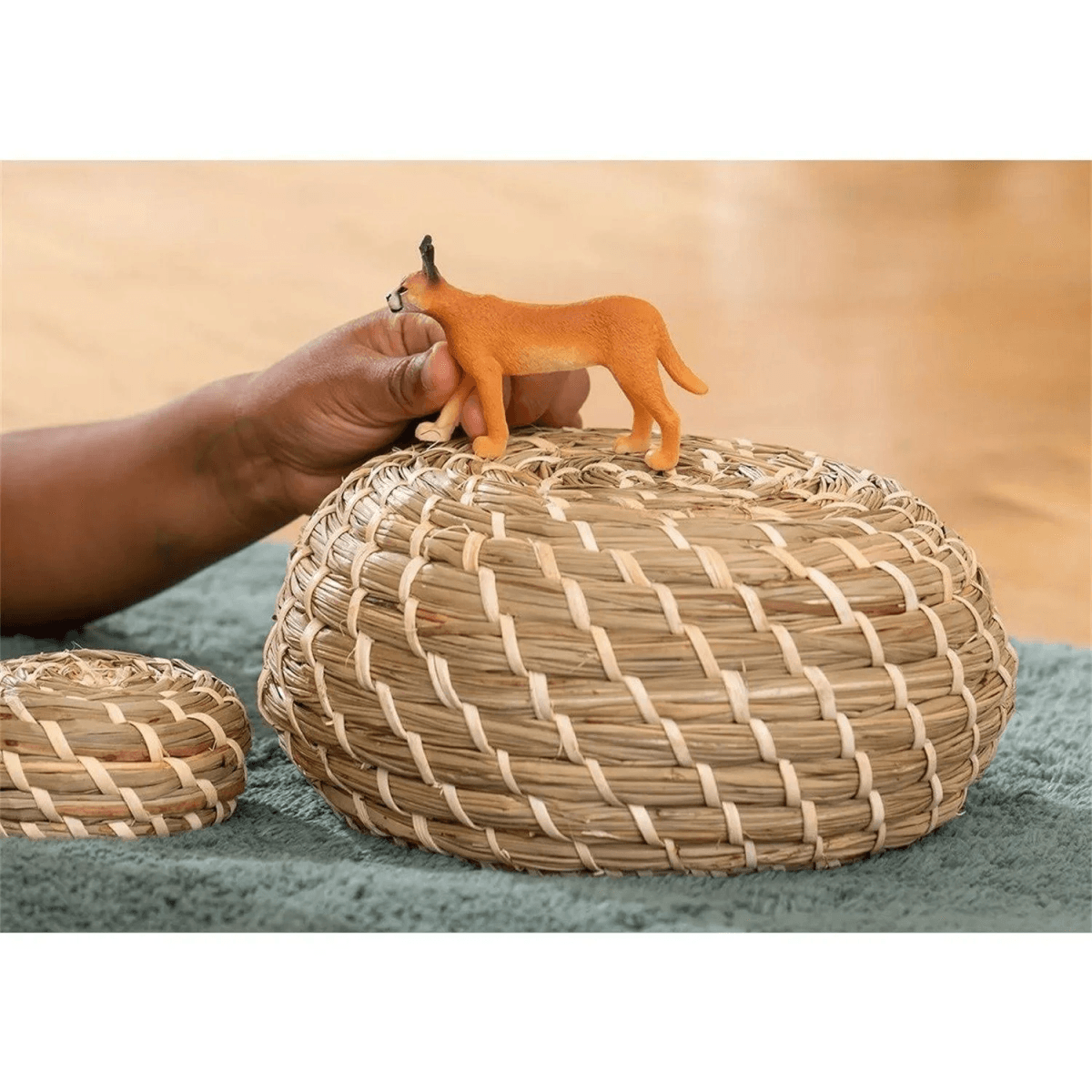 Una figurina di gatto selvatico arancione si trova su un cesto intrecciato tenuto da una mano.