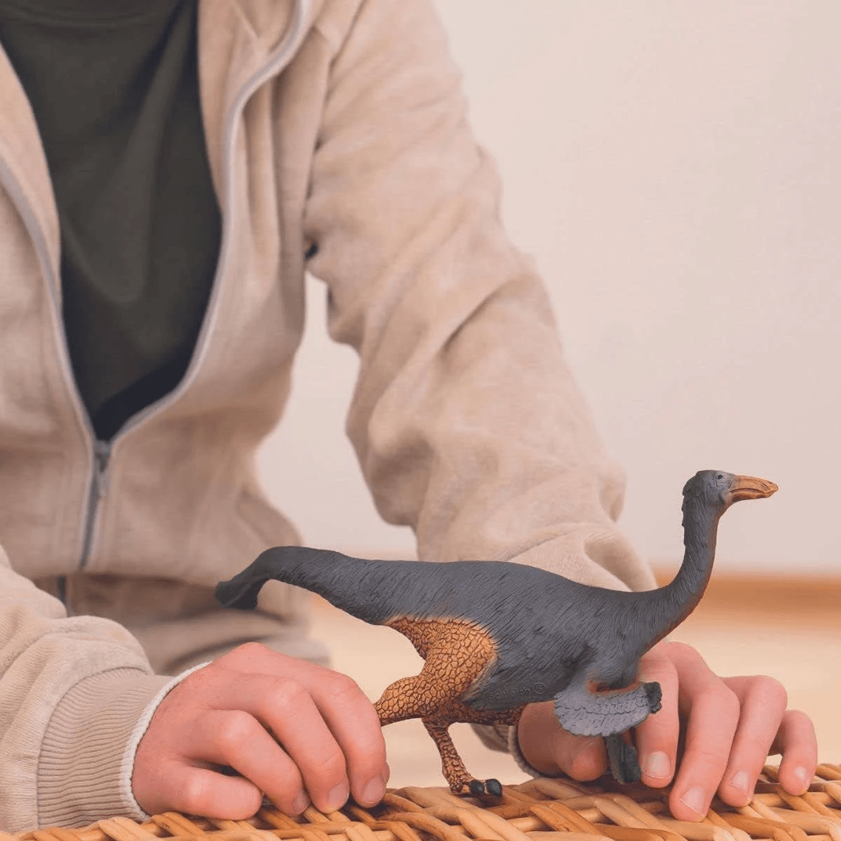 Una persona con felpa beige tiene un giocattolo dinosauro grigio scuro con zampe arancioni.
