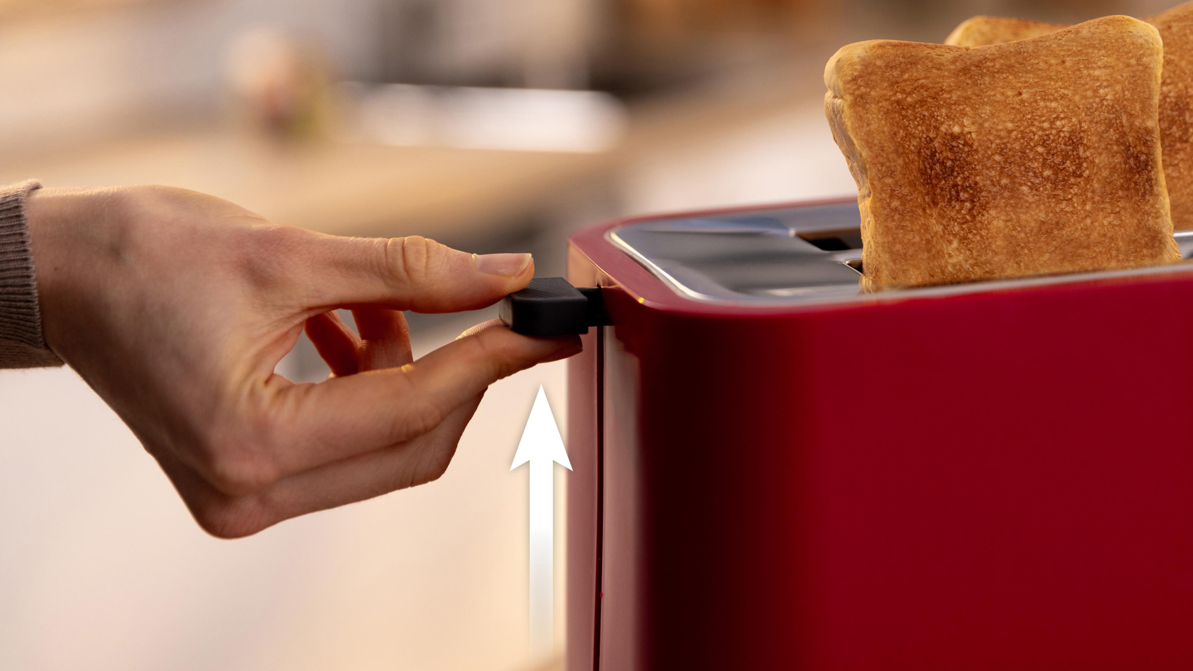 Eine Hand drückt den Hebel eines roten Toasters nach unten.