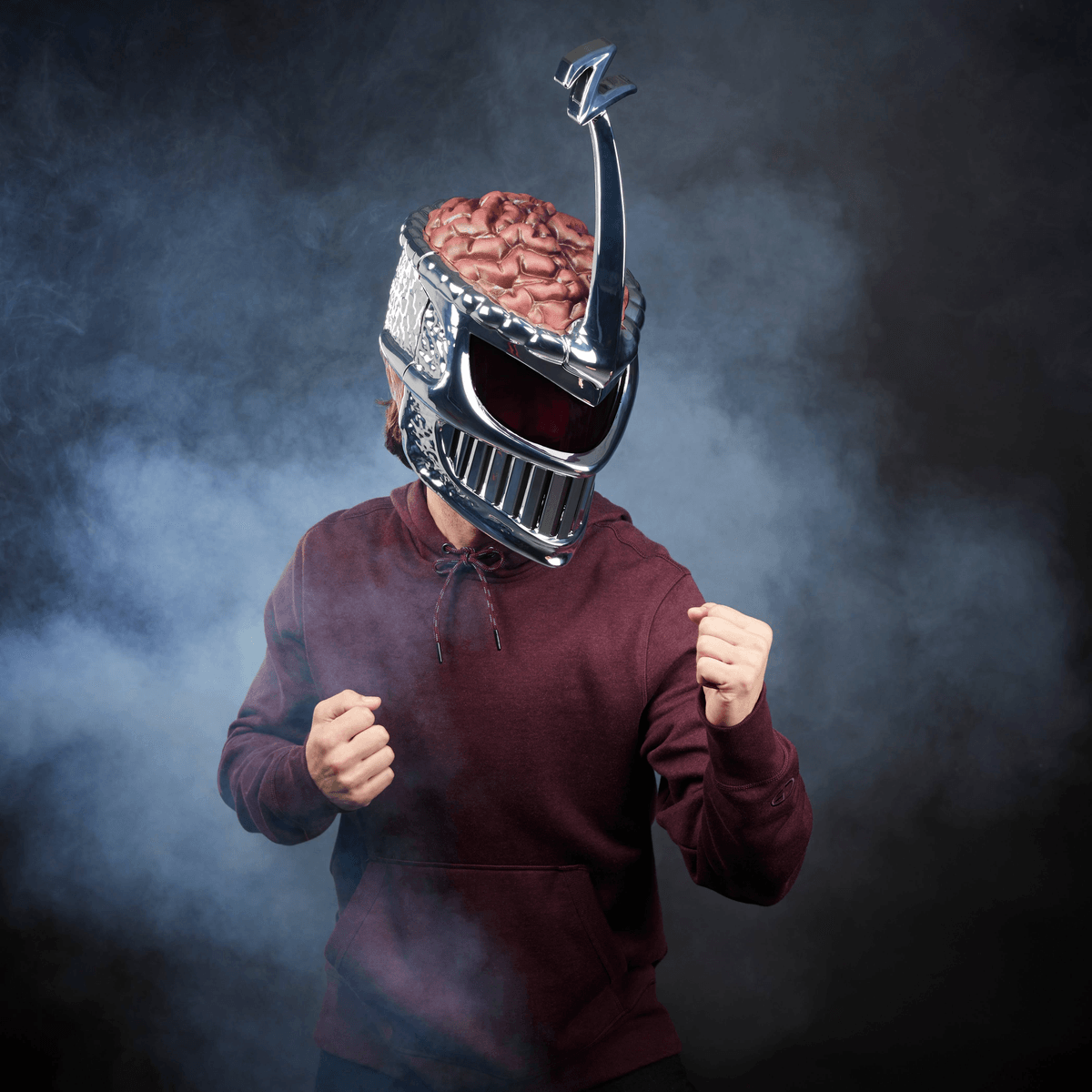 Bordo kapüşonlu kişi, beyinli gümüş kask takıyor. Sis etrafı sarıyor.