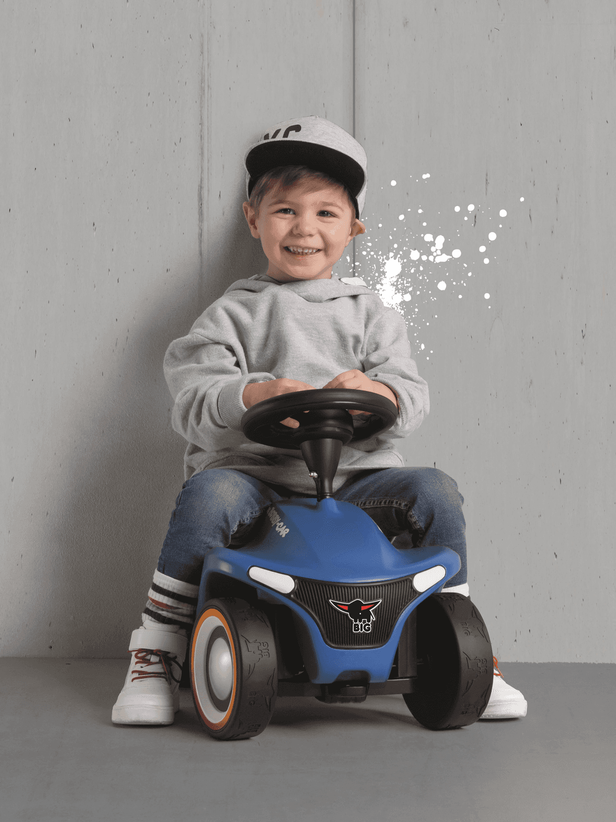 Un niño con vaqueros y sudadera se sienta en un coche de juguete azul.