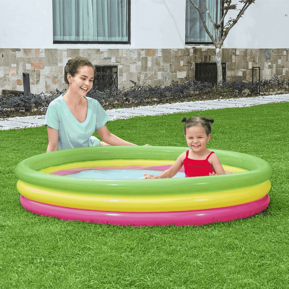Frau und Kind planschen im bunten aufblasbaren Pool im Garten.