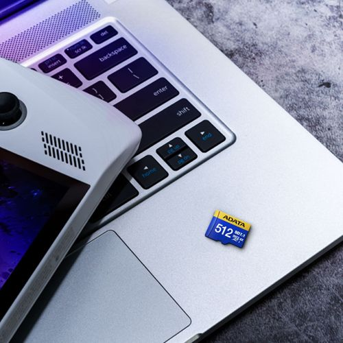 Une puce mémoire bleue de 512 Go repose sur le clavier d'un ordinateur portable à côté d'un appareil portable blanc.