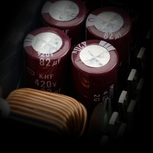 Quattro condensatori bordeaux da 82 µF, 420V, e una bobina di rame su un circuito stampato scuro.