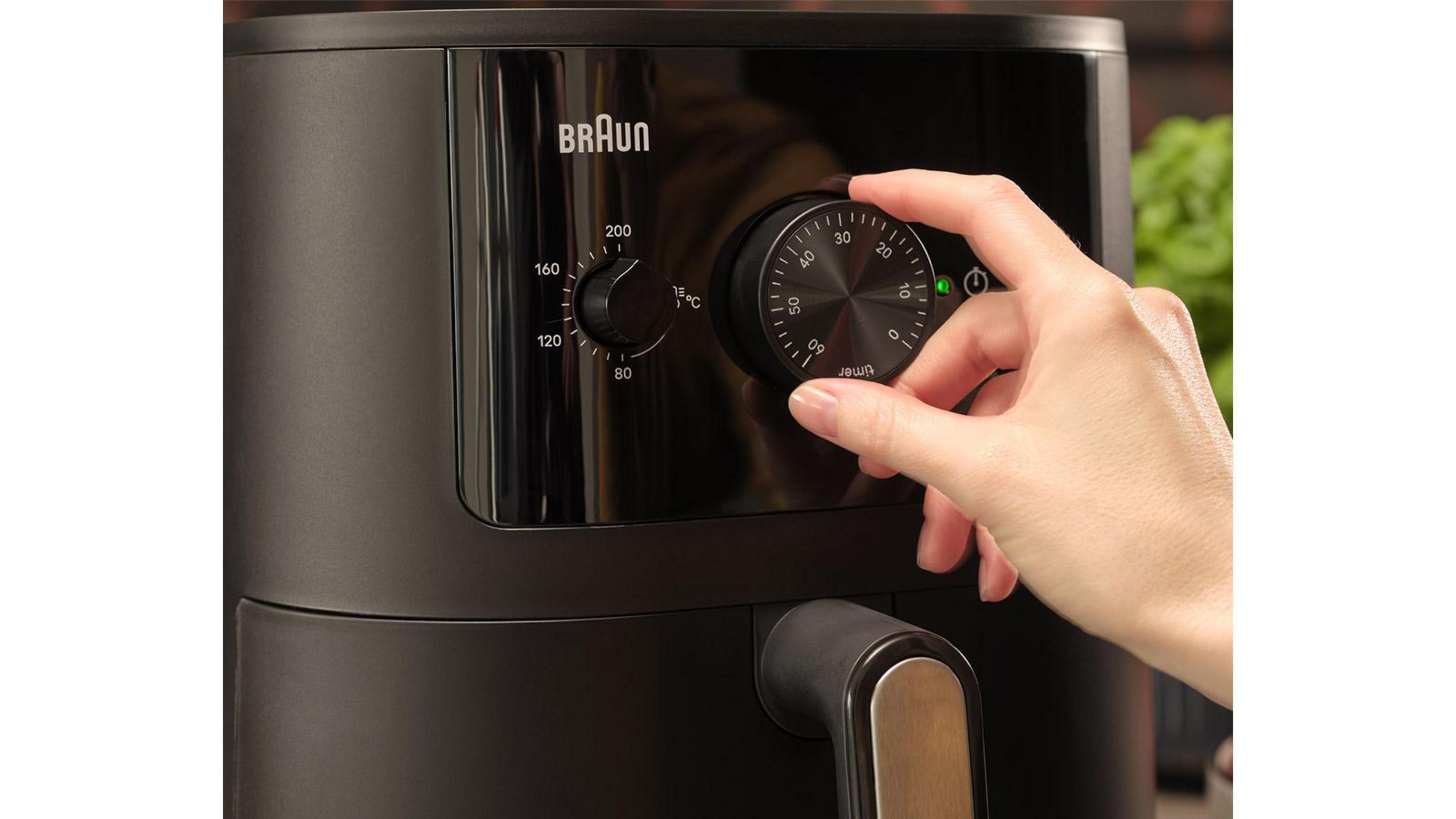 Una mano gira la manopola del timer su un pannello di controllo di una friggitrice ad aria Braun nera.