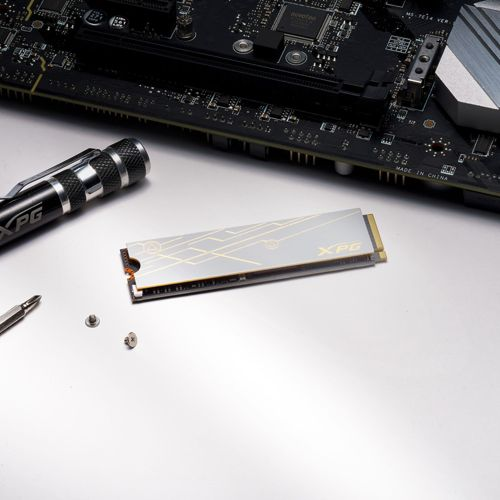 Een zilveren XPG SSD, schroevendraaier en schroeven op een moederbord.