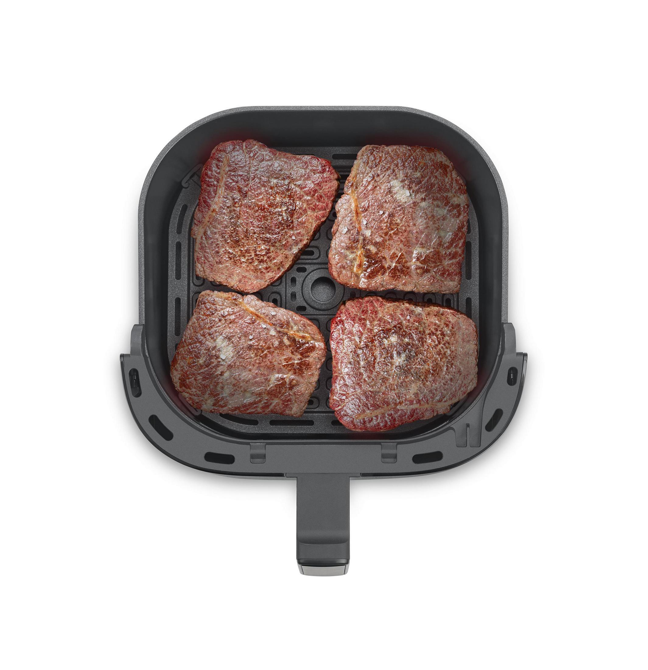 Vier angebratene Steaks in einem schwarzen Airfryer-Korb auf weißem Hintergrund.