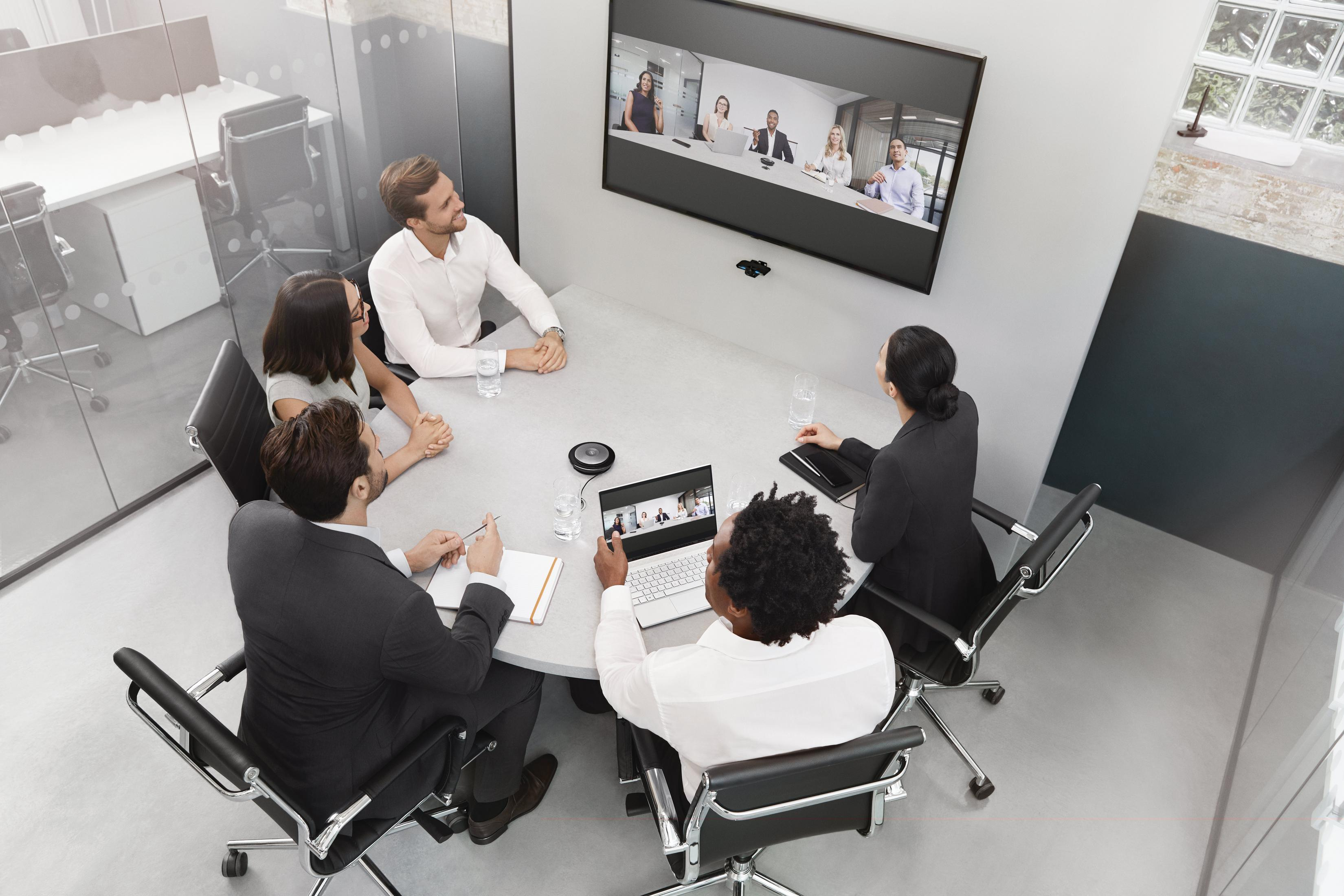 Persone in una sala conferenze con un grande schermo che mostra una videoconferenza.