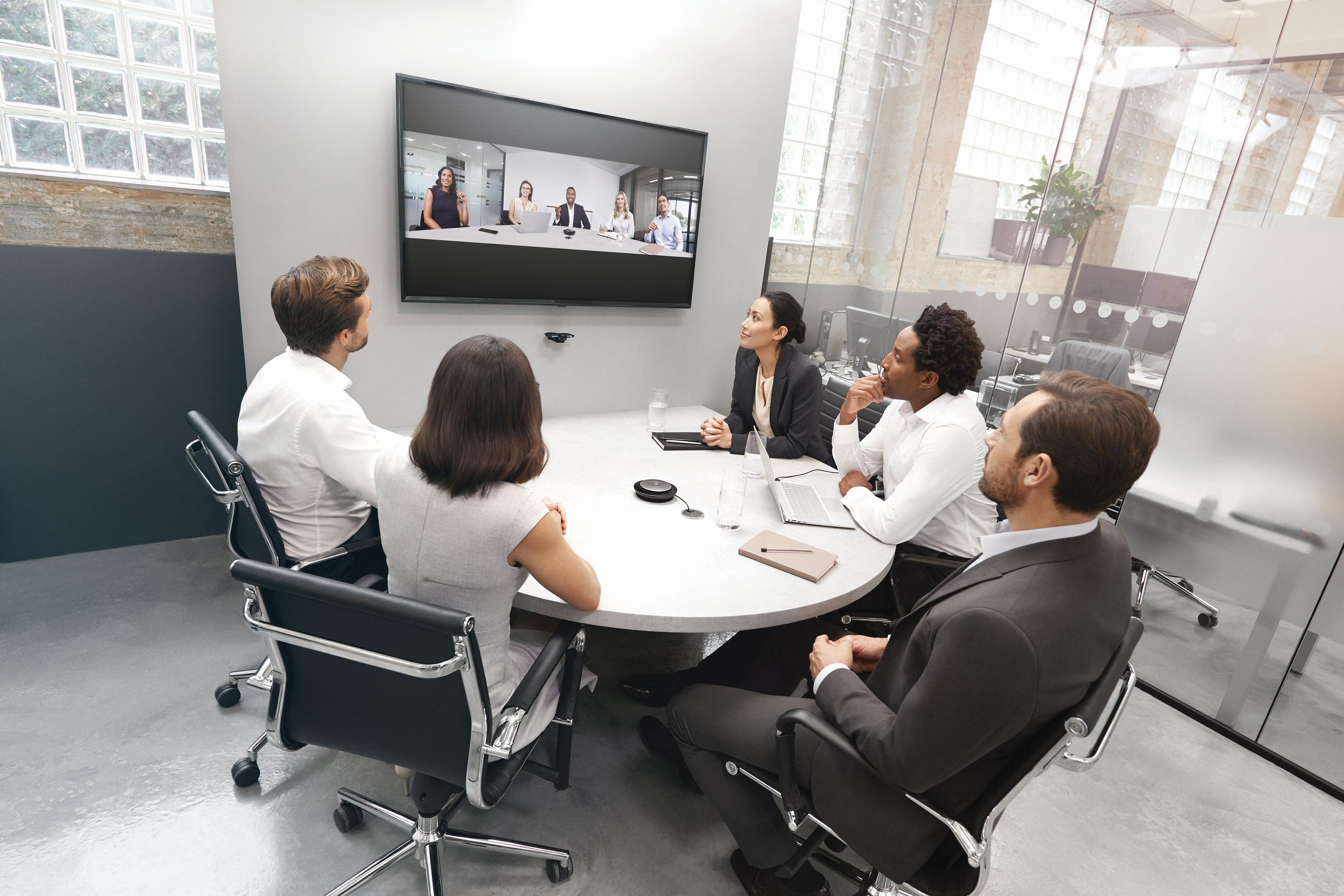 Persone in videoconferenza in ufficio. Diverse persone sedute attorno a un tavolo.