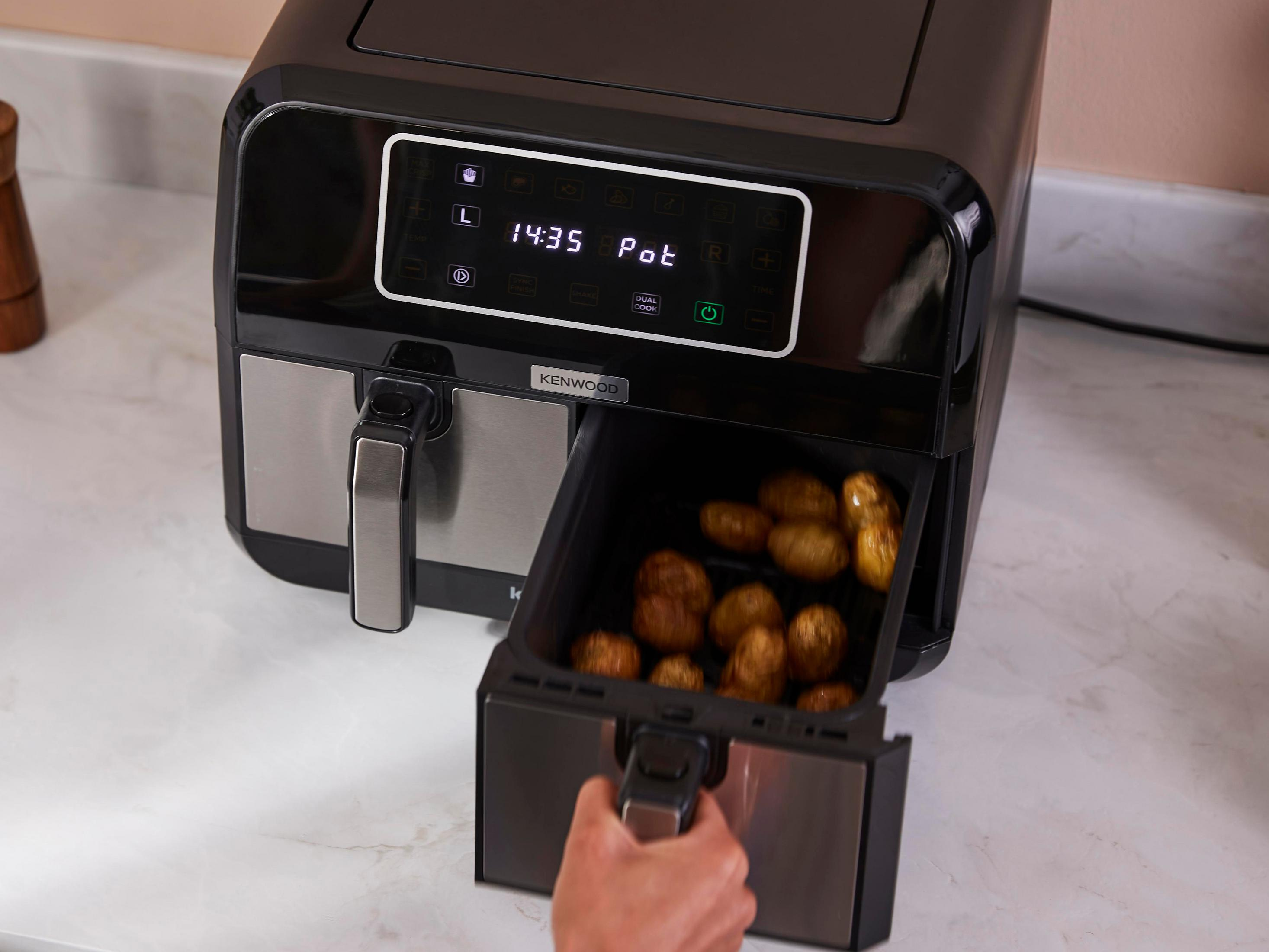 Una friggitrice ad aria nera con cestello estratto, pieno di patate.