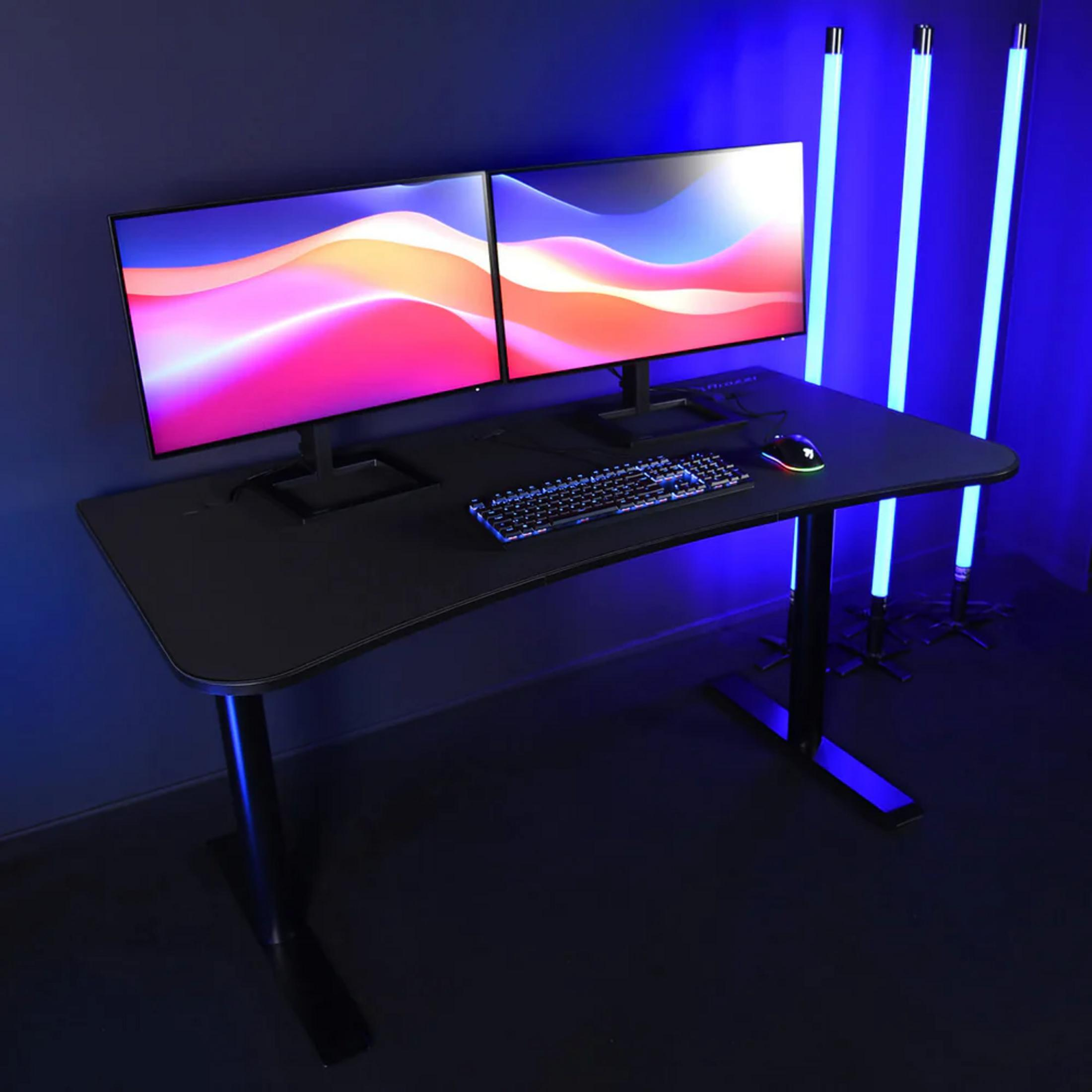 Una scrivania nera con due monitor, tastiera e mouse, illuminata da luci blu.
