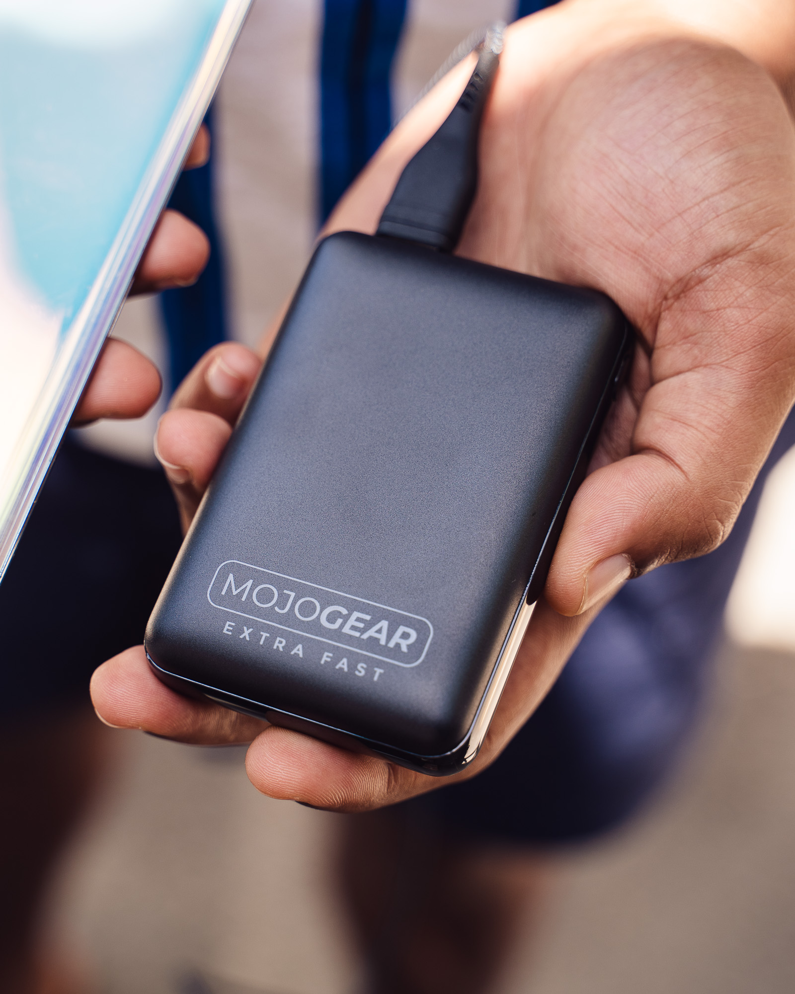 Eine Hand hält eine schwarze MojoGear Powerbank, die mit einem Gerät verbunden ist.