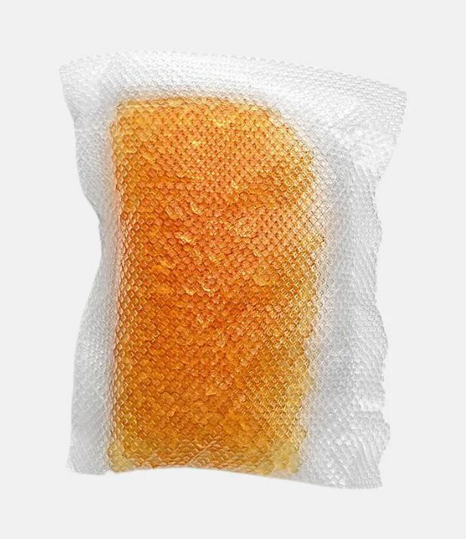 Una esponja naranja con una superficie de red blanca sobre un fondo gris.