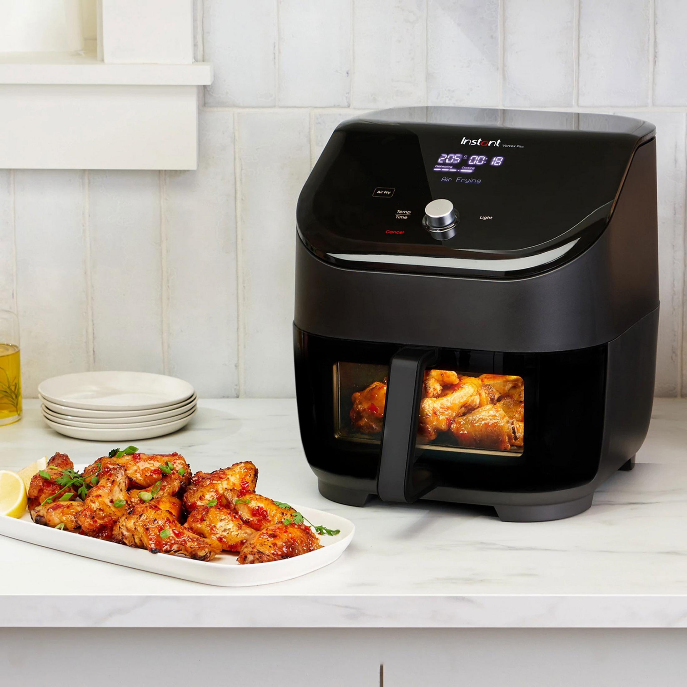 Black Instant Vortex Plus air fryer with cooked chicken wings on a plate.