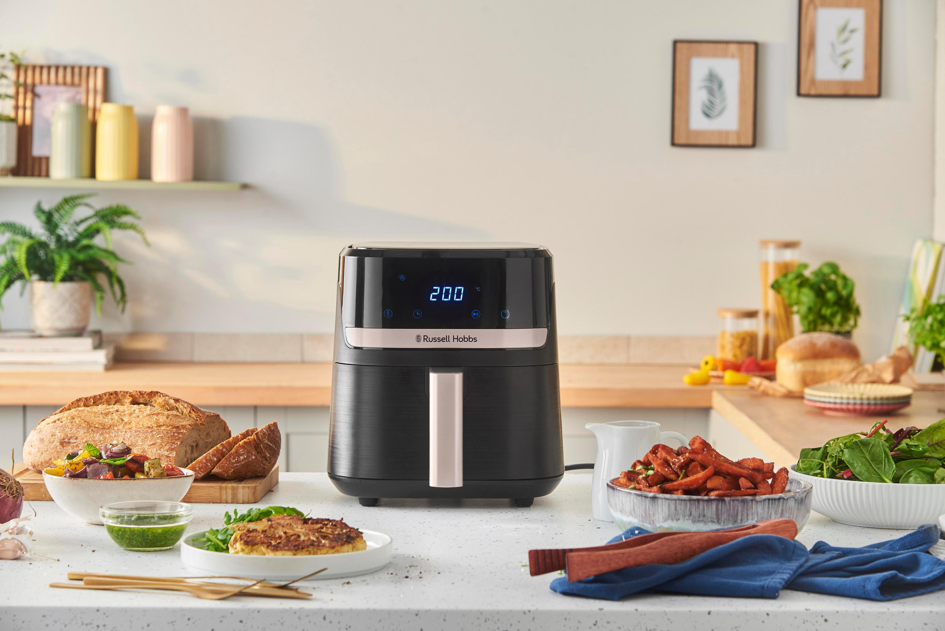 Een zwarte airfryer staat op een aanrecht met eten.