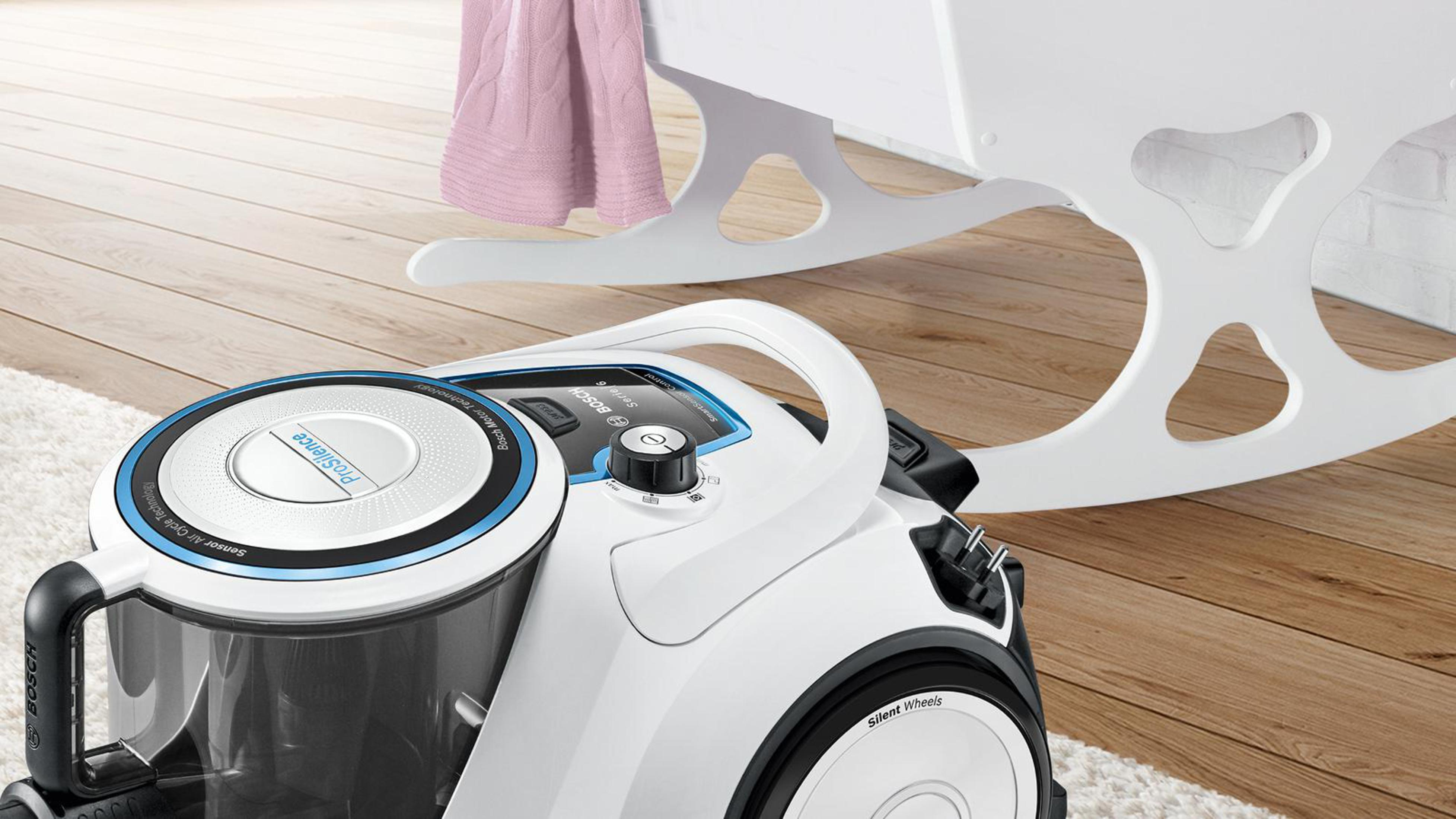 Weißer Bosch Staubsauger mit blauen Akzenten neben einem weißen Kinderbett.