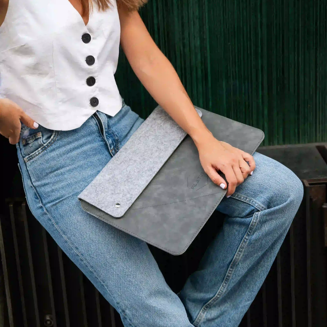 Una donna in jeans e gilet bianco tiene una custodia per laptop grigia.