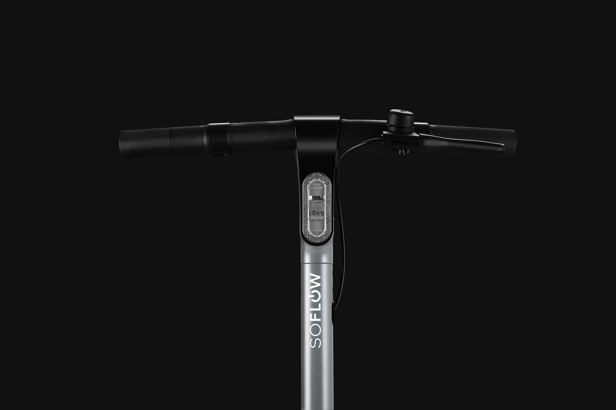 Lenker eines E-Scooters mit beleuchtetem Logo und Griffen vor schwarzem Hintergrund.