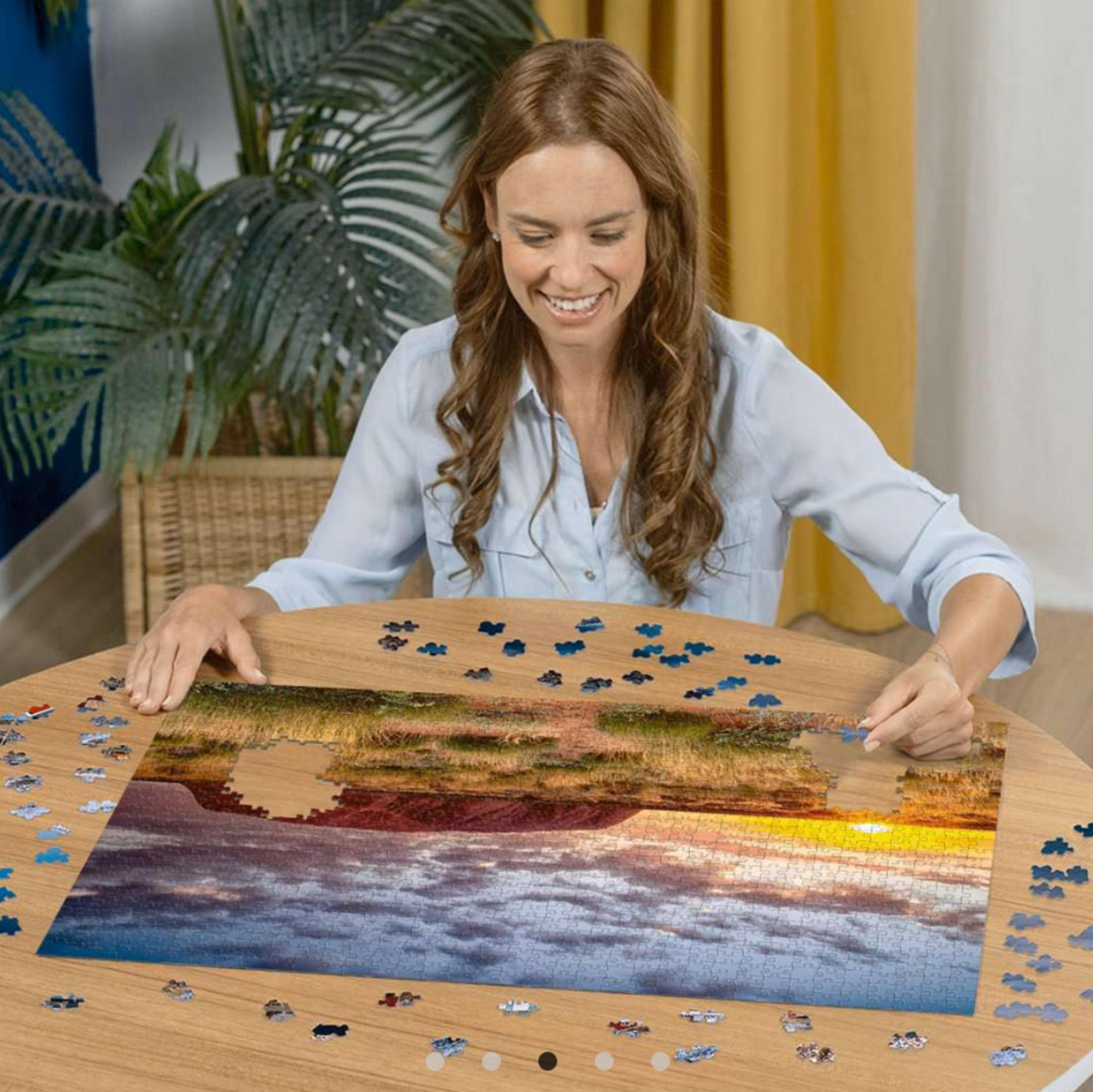 Frau vervollständigt ein Puzzle mit Sonnenuntergang über dem Wasser.
