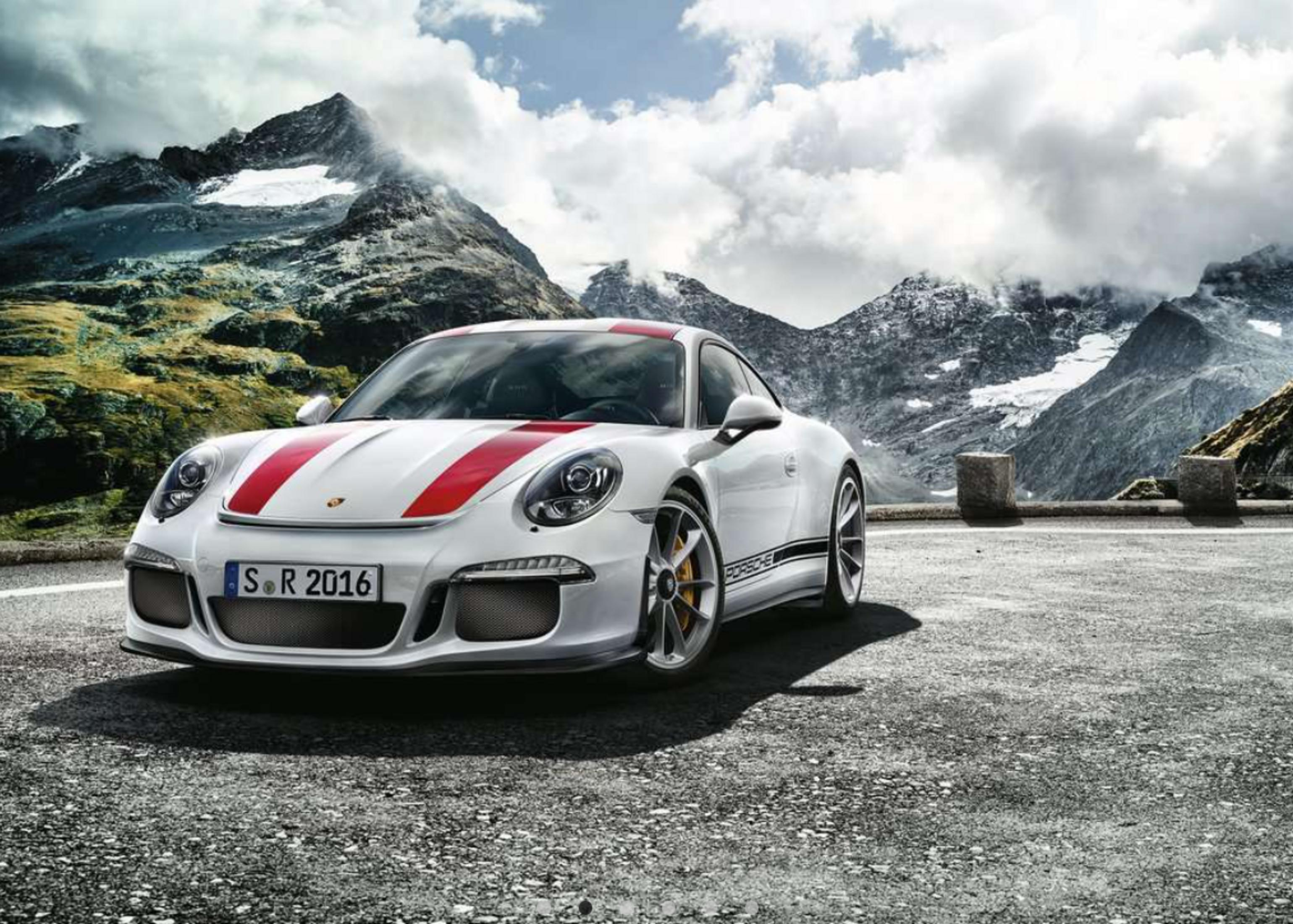 Une Porsche blanche à rayures rouges est sur une route asphaltée devant un paysage montagneux.