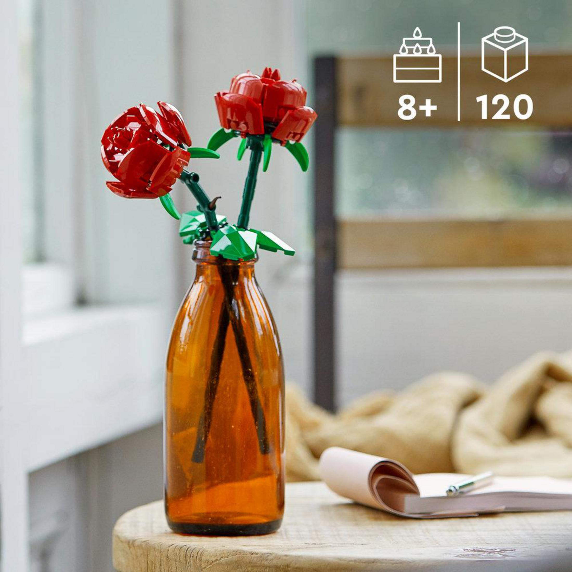 Dos rosas rojas de Lego en una botella marrón sobre una mesa de madera.