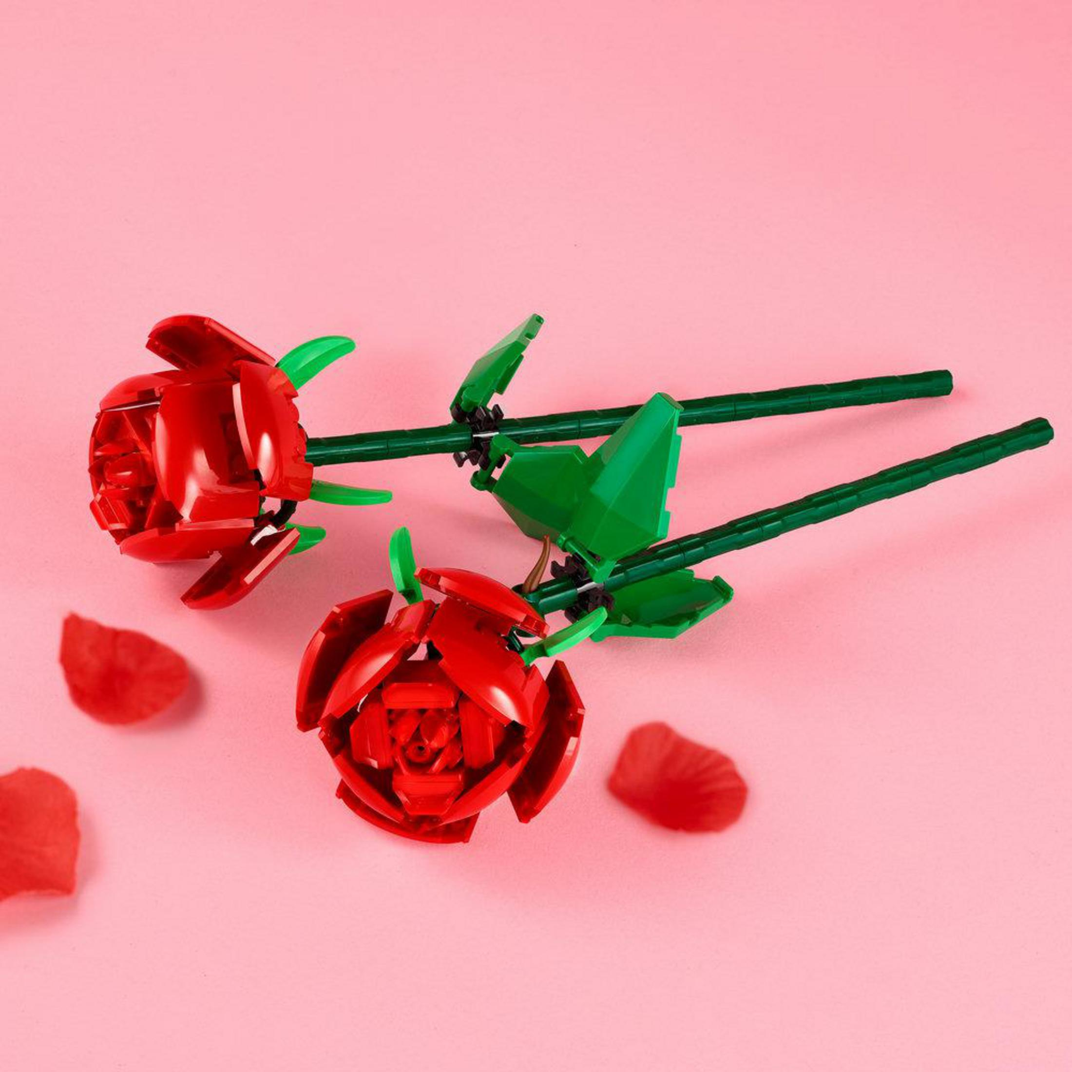 Dos rosas rojas de Lego con tallos y hojas verdes sobre fondo rosa.