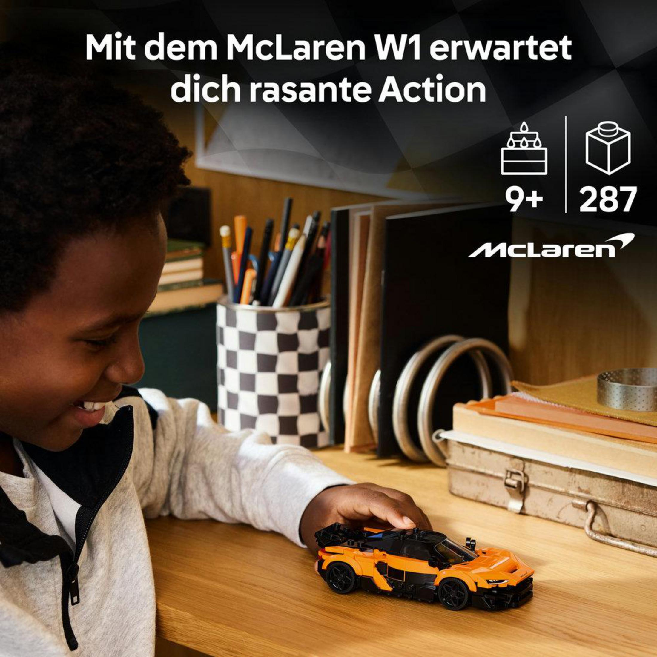 Bir çocuk ahşap bir masada turuncu Lego McLaren arabasıyla oynuyor.