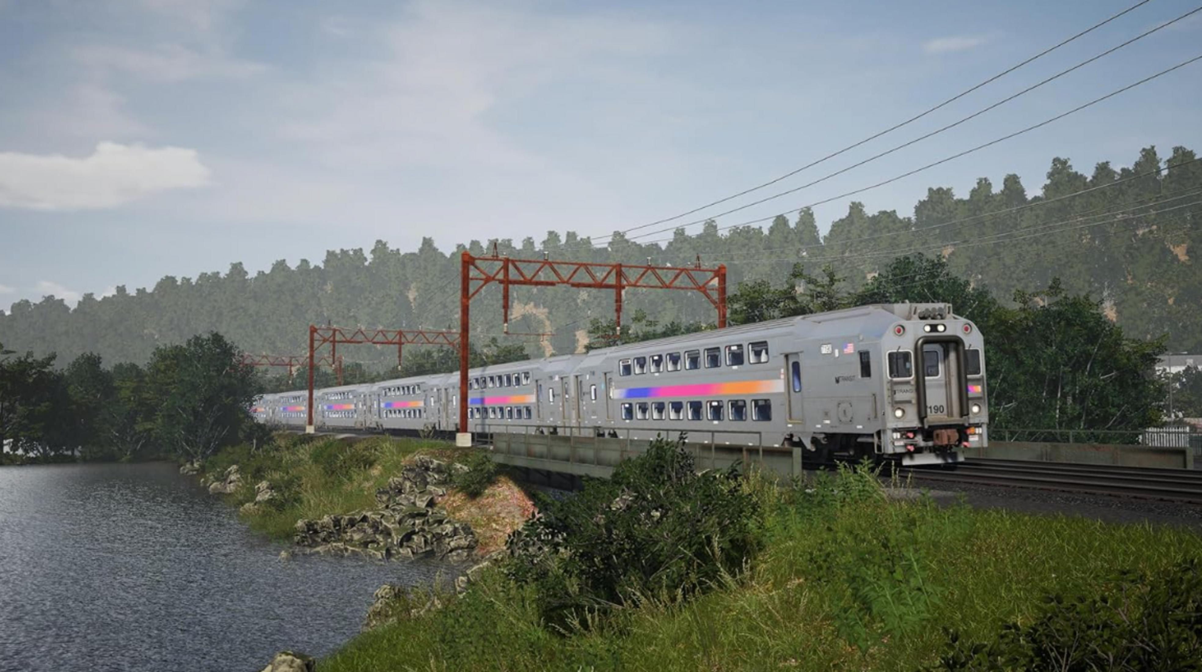 Un treno grigio viaggia su un ponte sopra un fiume, circondato da alberi.