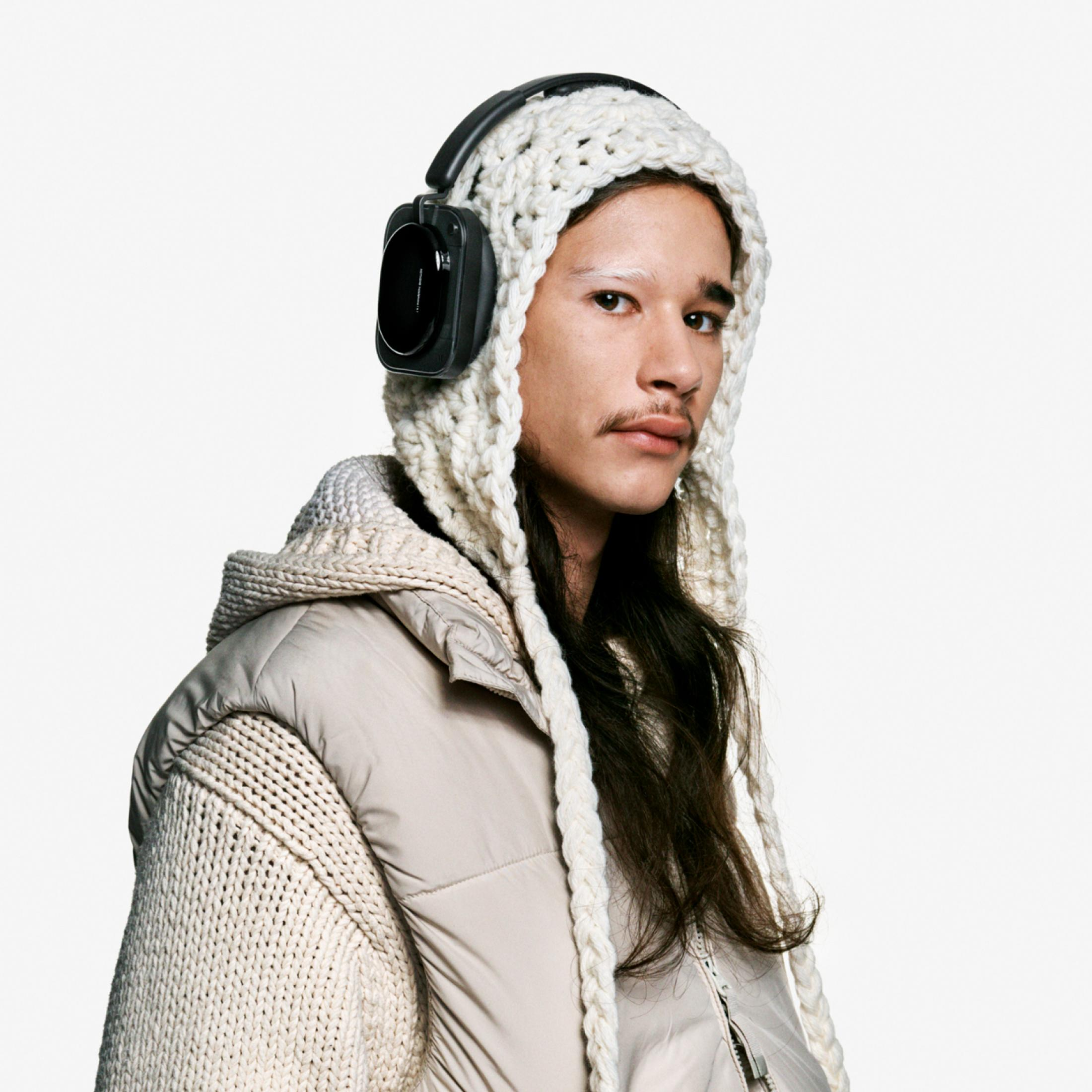 Un uomo con cuffie e cappello di lana, vestito con una giacca imbottita beige.