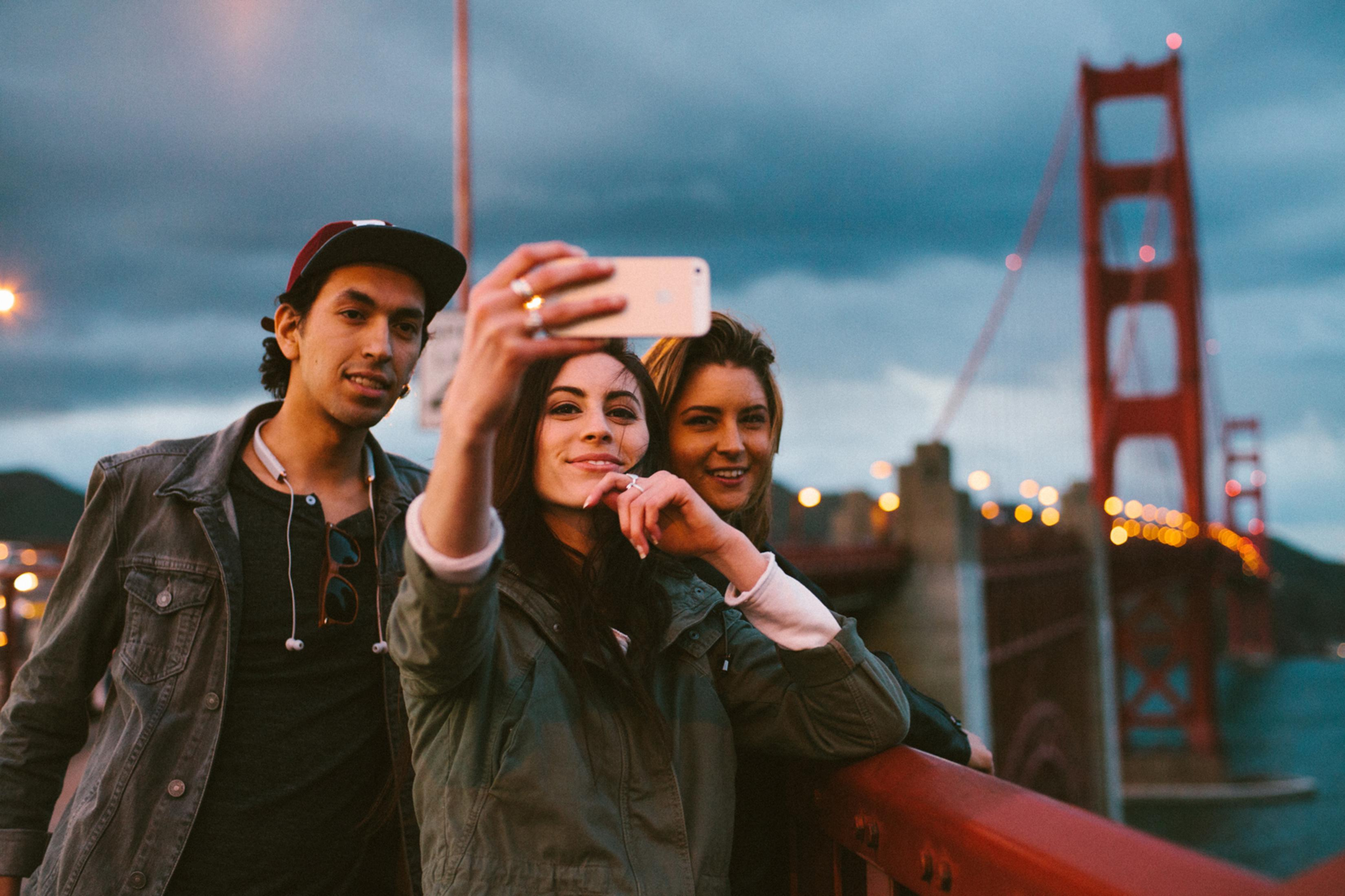 Tre amici si scattano un selfie davanti al Golden Gate Bridge al crepuscolo.