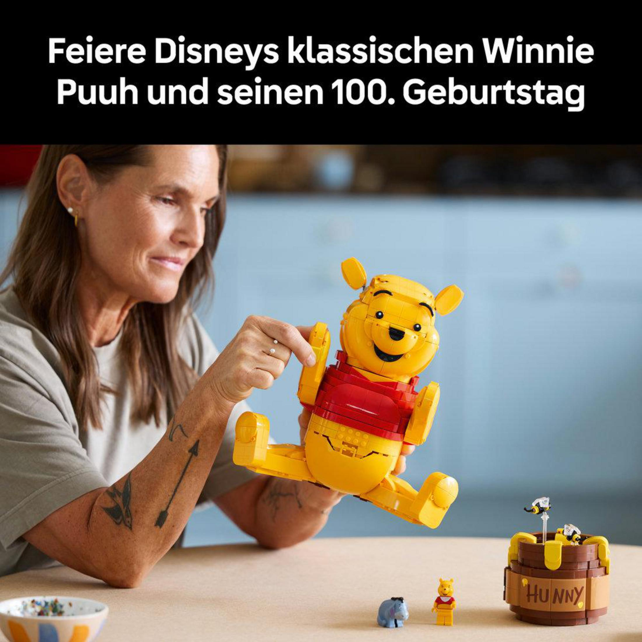 Una mujer sostiene una figura de Winnie Pooh de LEGO cerca de una olla de miel y figuras.