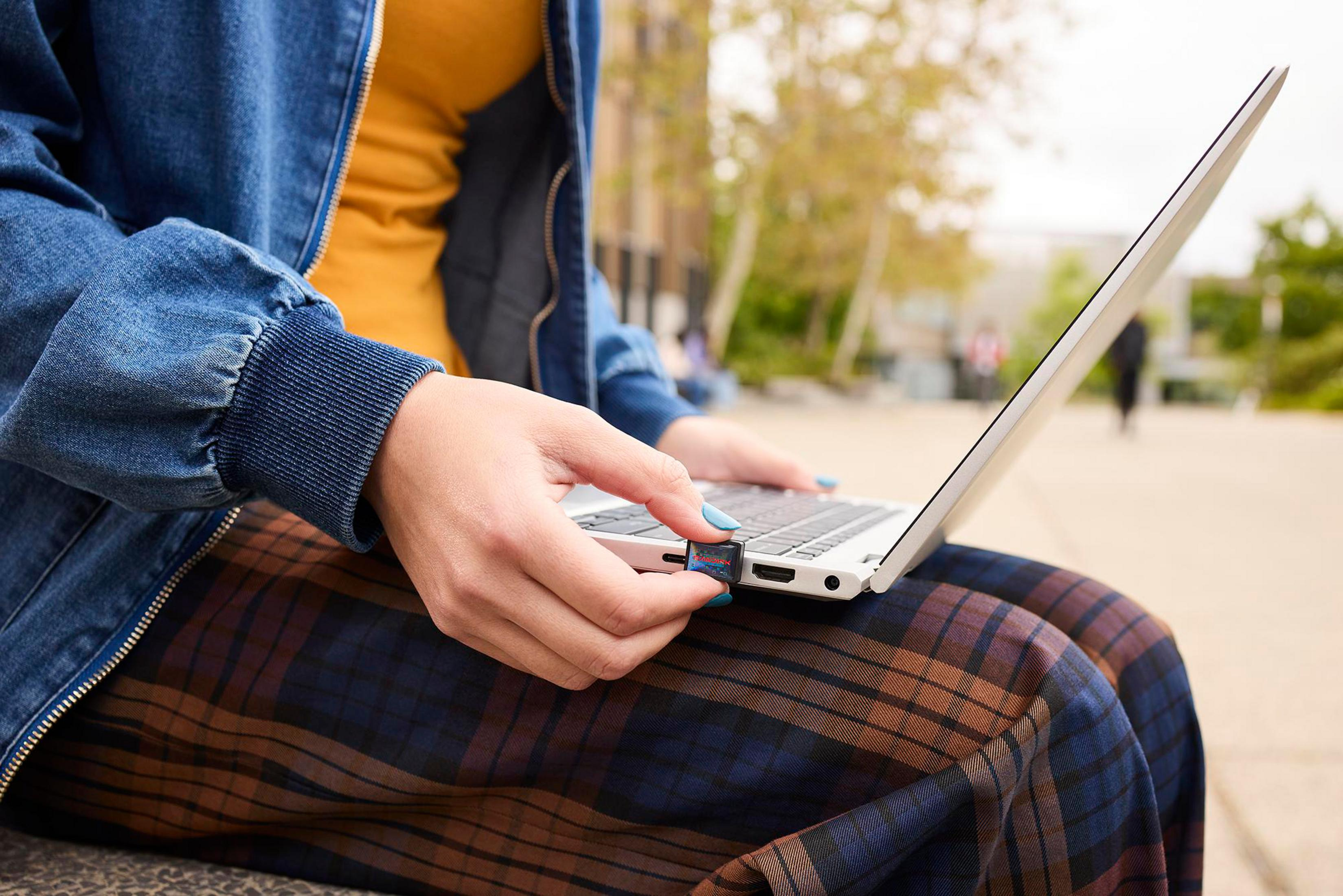 Una persona inserisce una chiavetta USB in un laptop all'aperto.