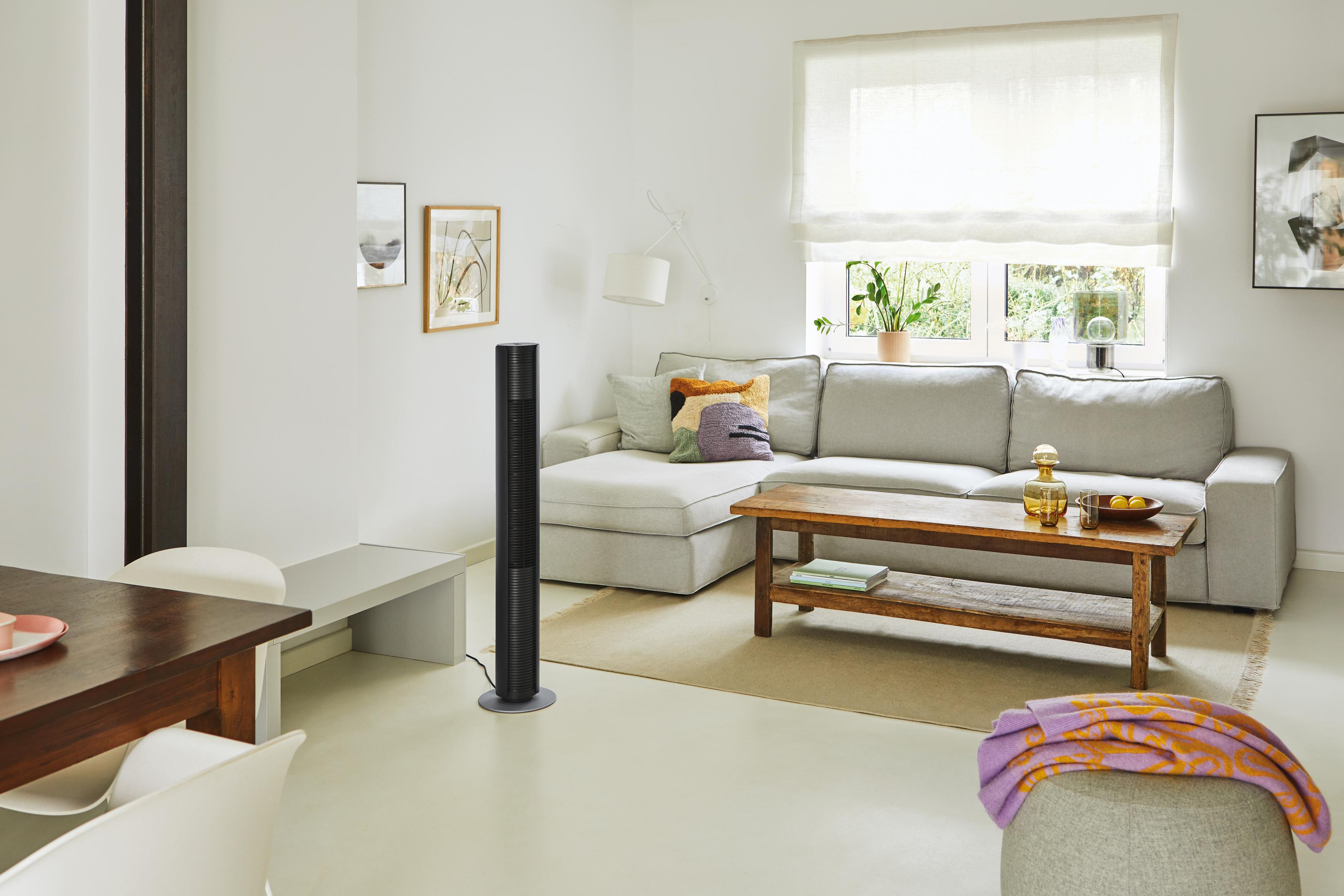 Ein Wohnzimmer mit Sofa, Couchtisch, Essbereich und einem Turmventilator.