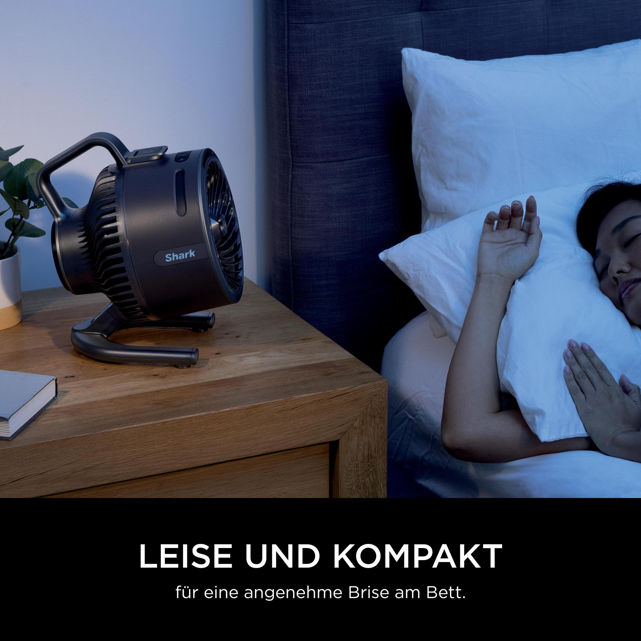 Een donkere Shark ventilator staat op een nachtkastje naast een slapend persoon.