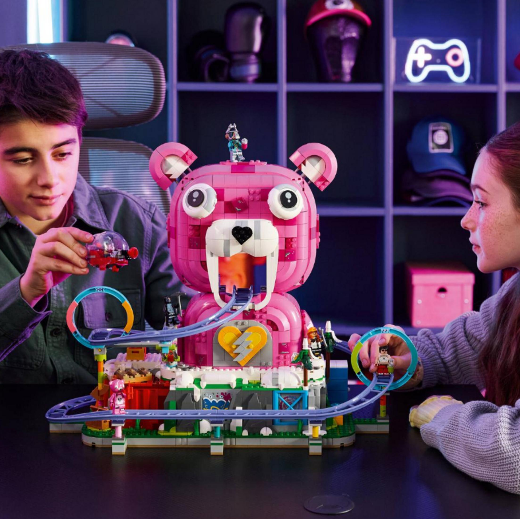 Çocuklar ayıcık başlı pembe Lego roller coaster yapıyor. Arkada neon ışıklar var.