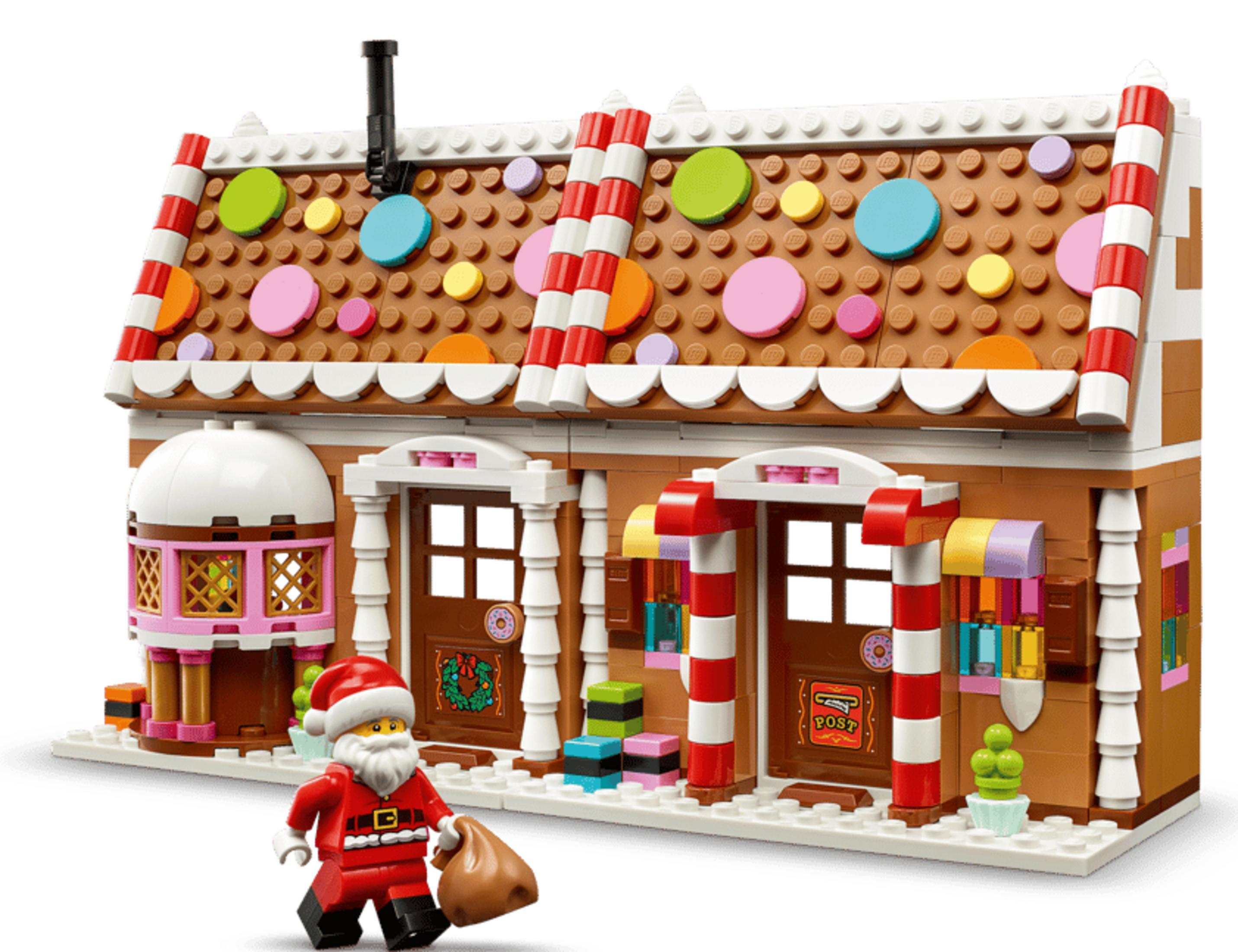 Çuvalı olan bir Lego Noel Baba, renkli şekerlerle süslenmiş zencefilli kurabiye evinin önünde duruyor.